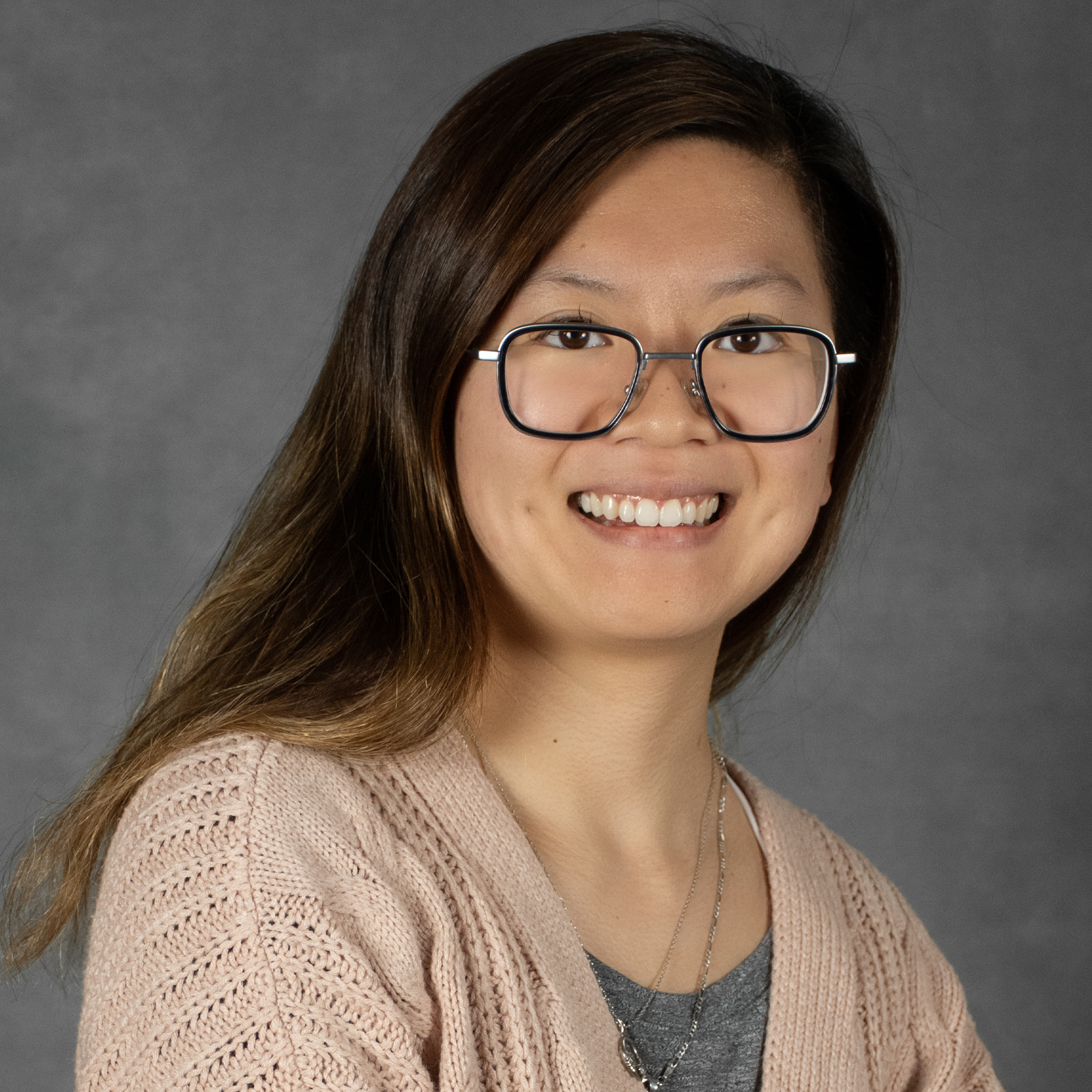 Woman with long dark hair wearing glasses, pink sweater and gray top