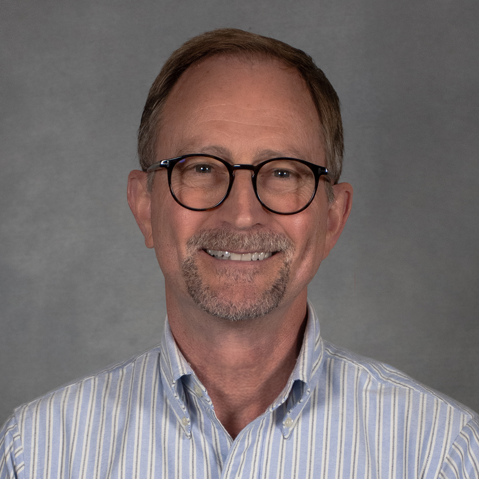 Man with short hair and goatee wearing a striped button-down shirt and glasses