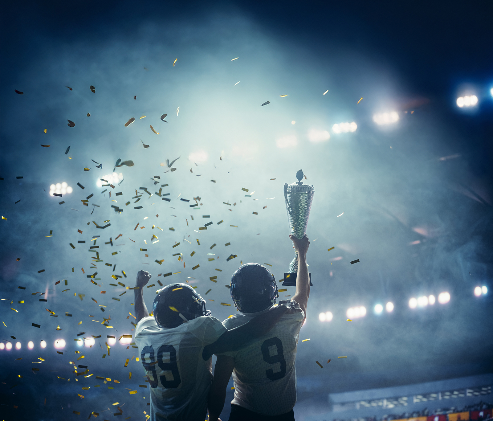 Two young football players celebrating their win while holding the trophy up