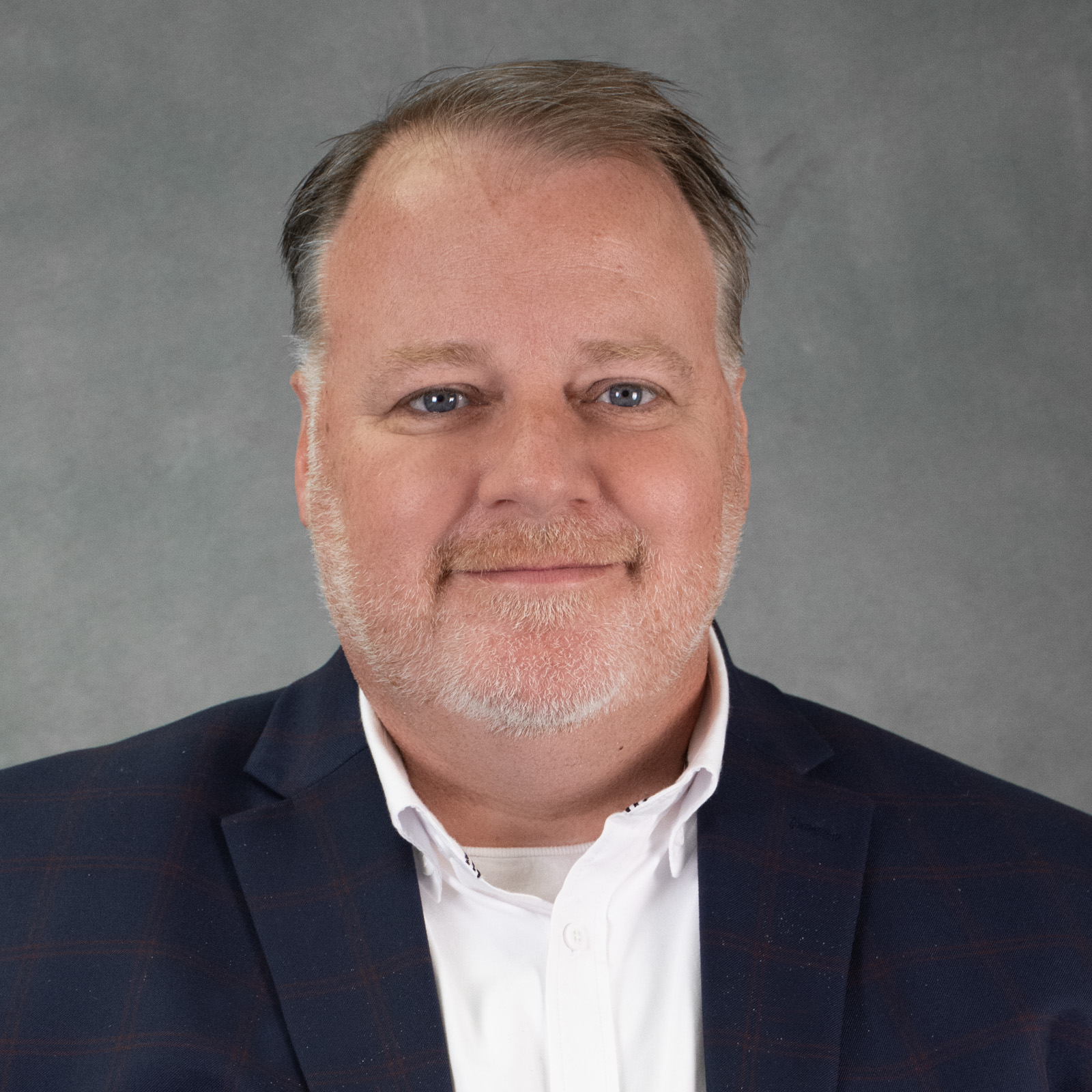 man with short brown hair and close cropped graying beard wearing navy blazer and white shirt