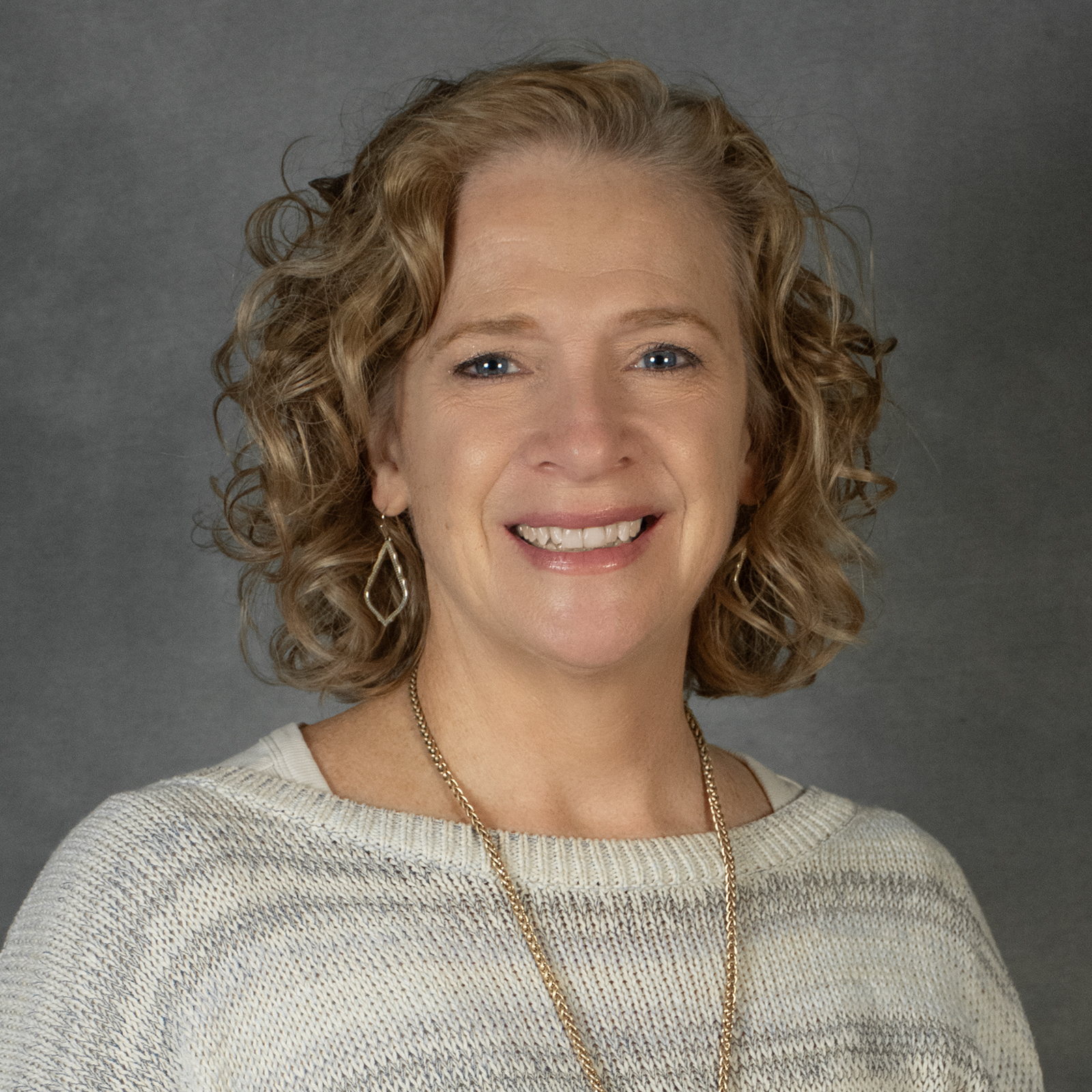 Woman with chin length blond wavy hair wearing a cream striped poncho