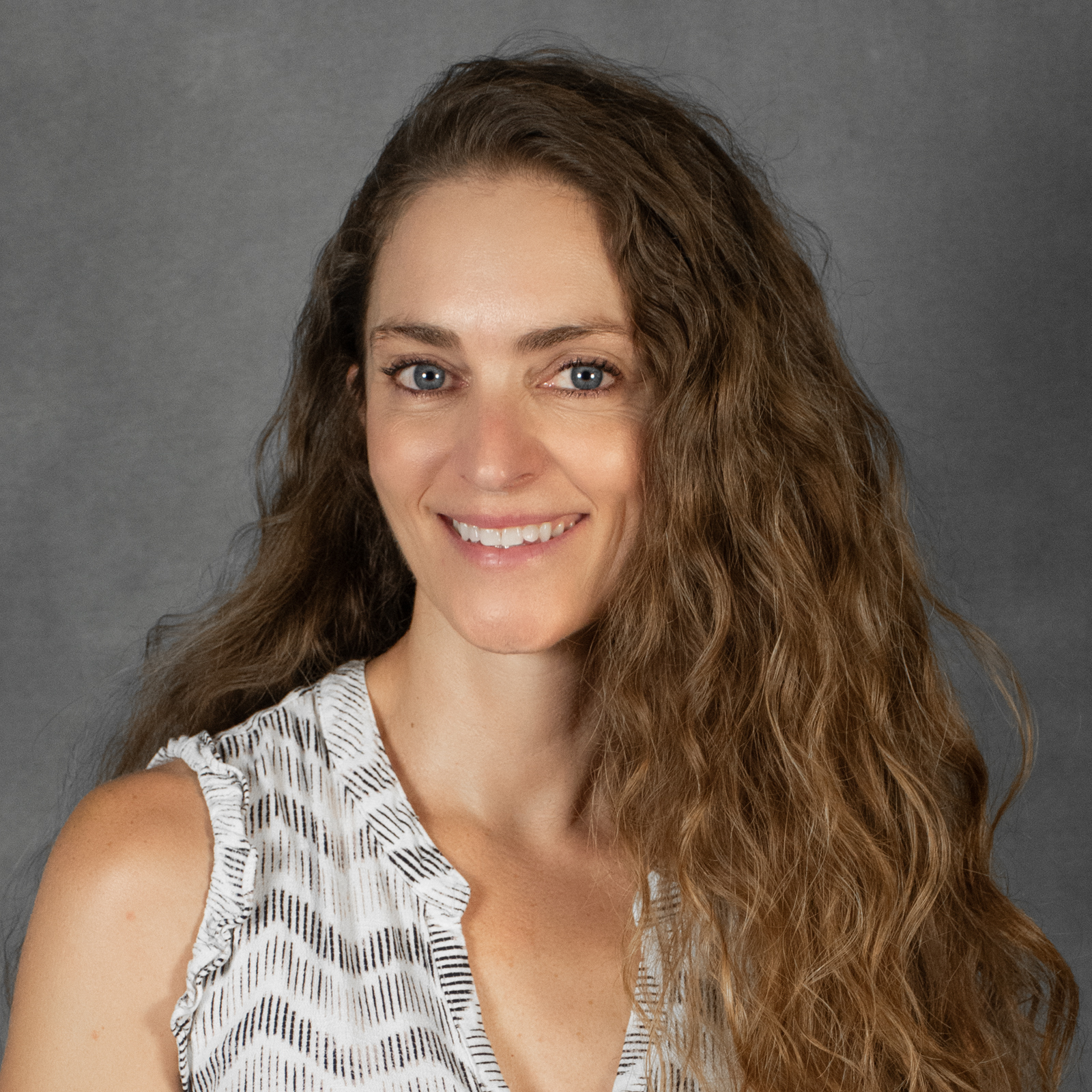 Woman with long brown wavy hair wearing a white print top