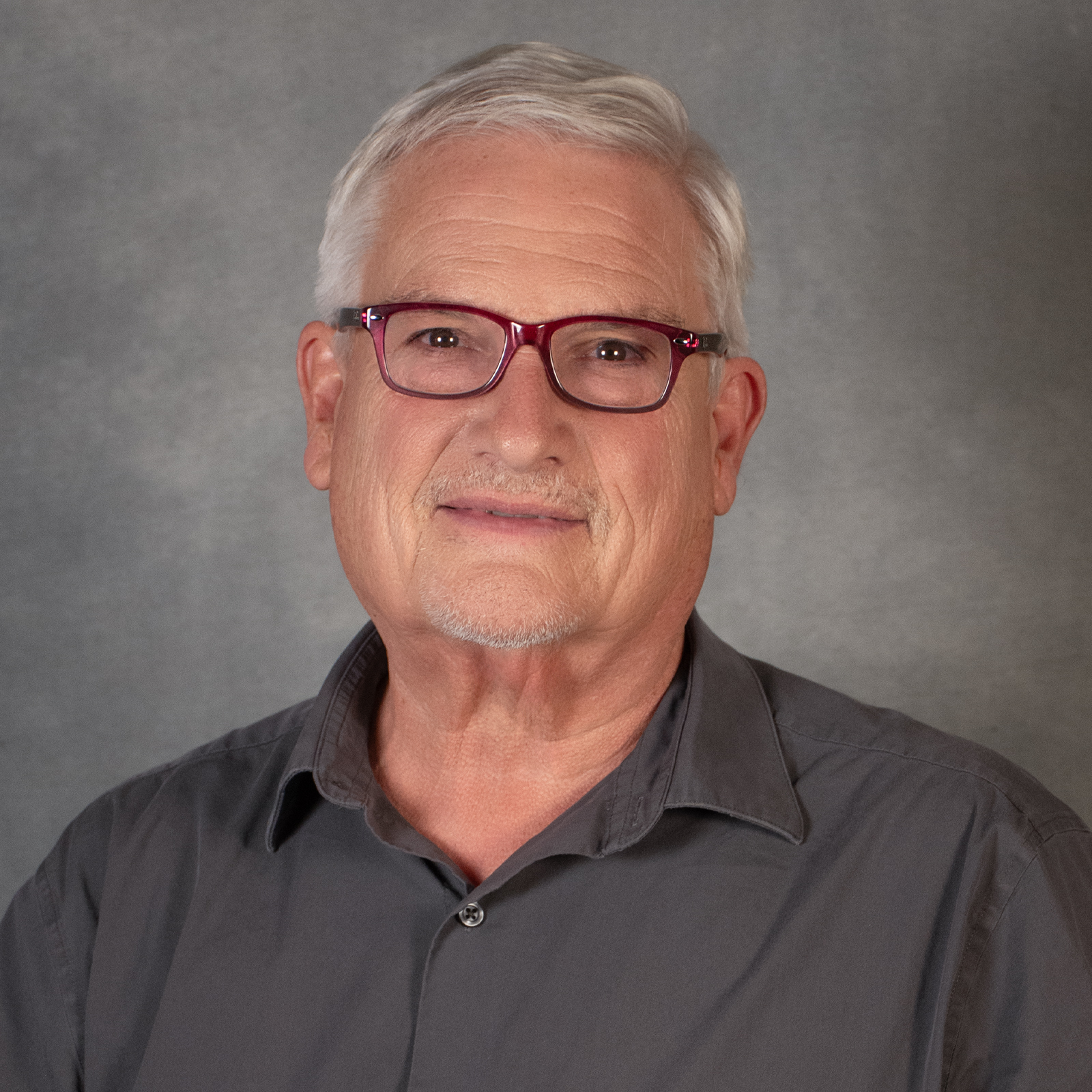 man with short gray hair wearing red glasses and gray shirt