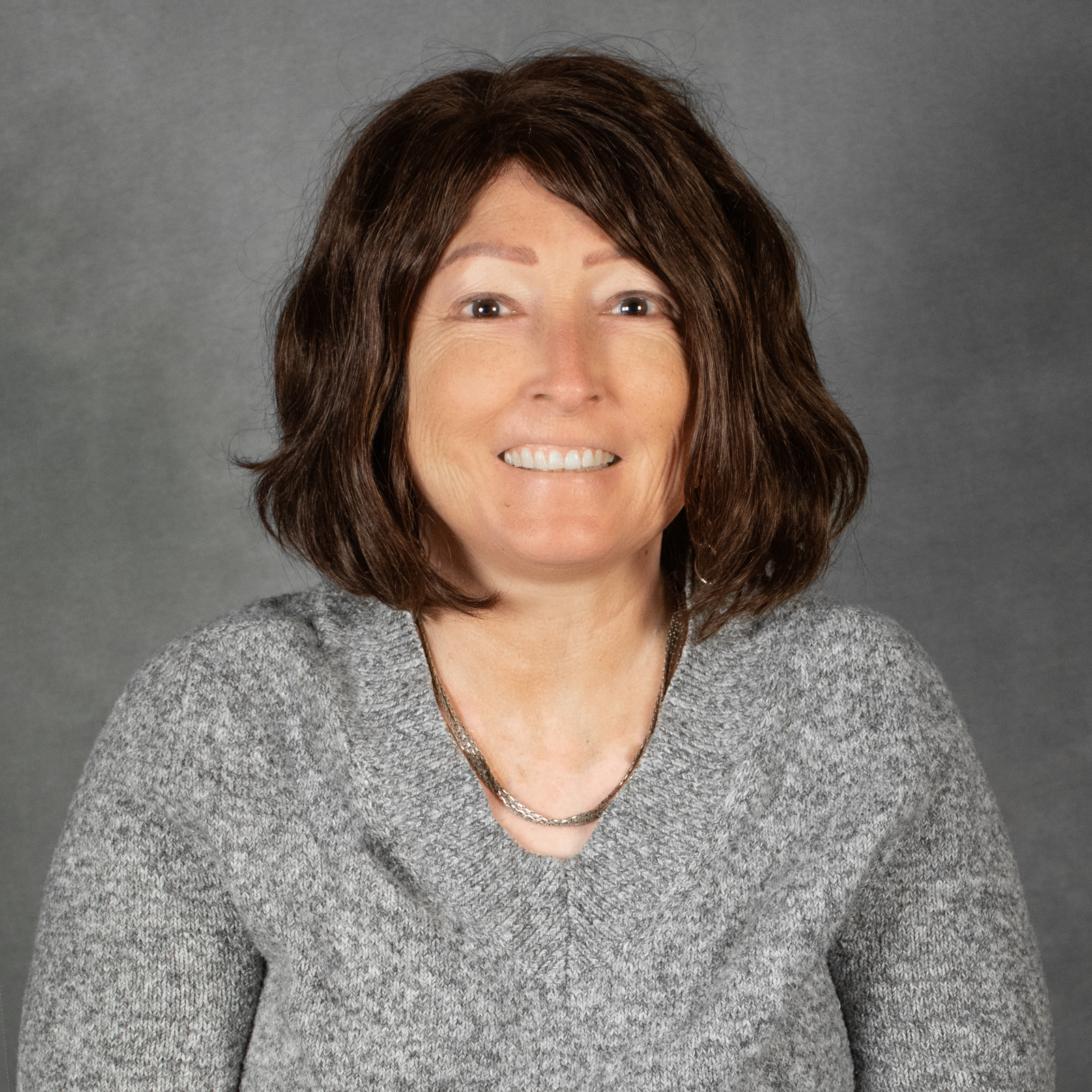 Woman with chin length auburn hair wearing a gray v-neck sweater