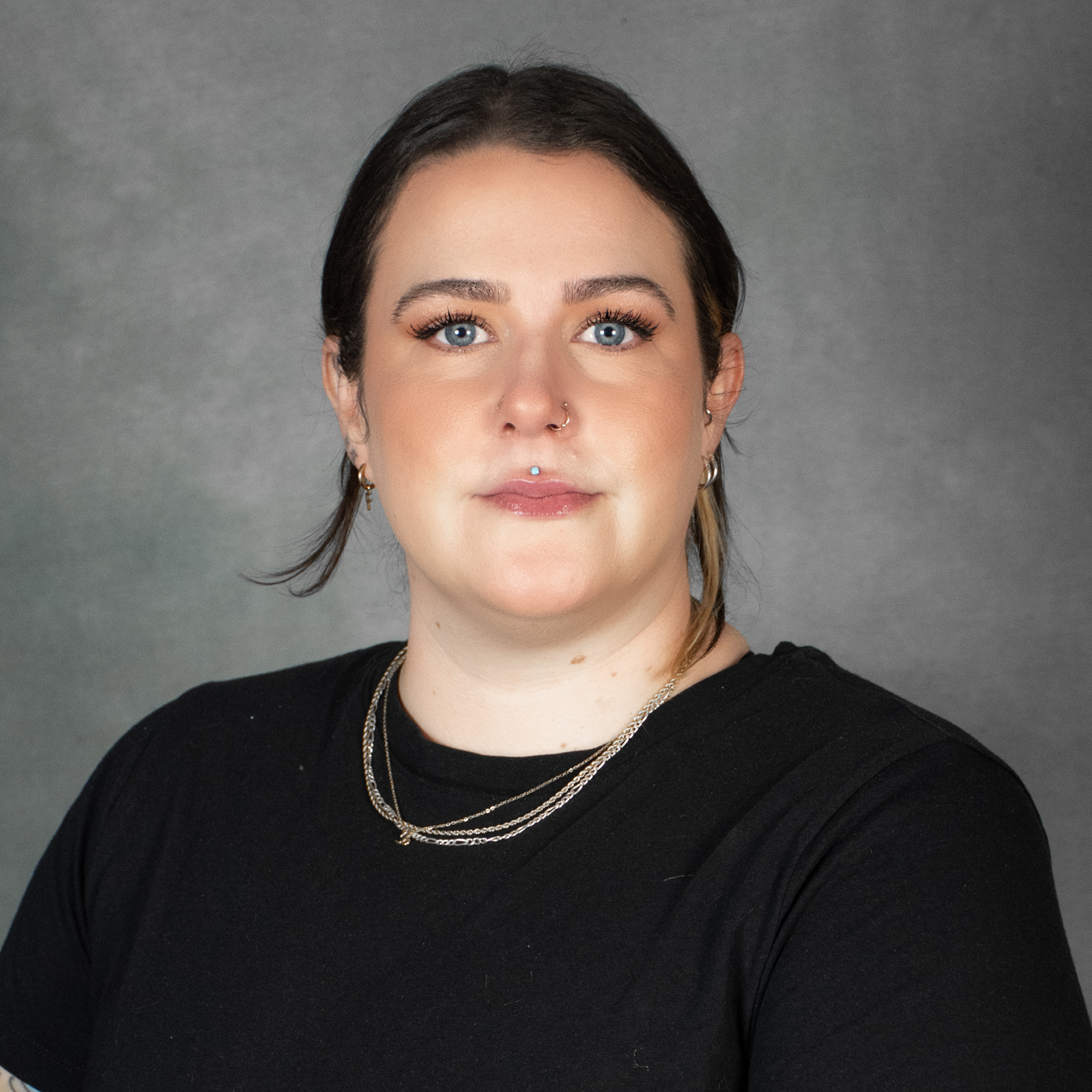 Woman with pulled back dark hair wearing a black top and gold necklace