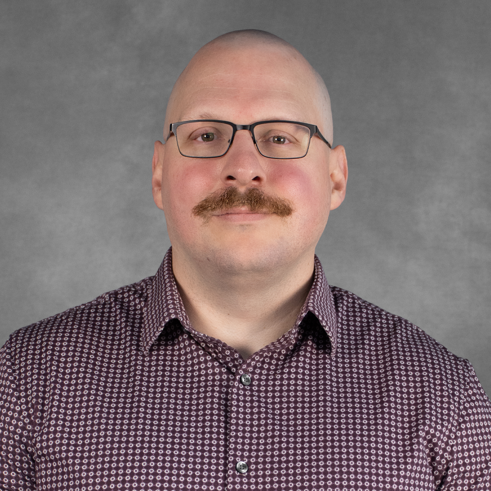 man with buzz cut wearing glasses and maroon shirt with collar