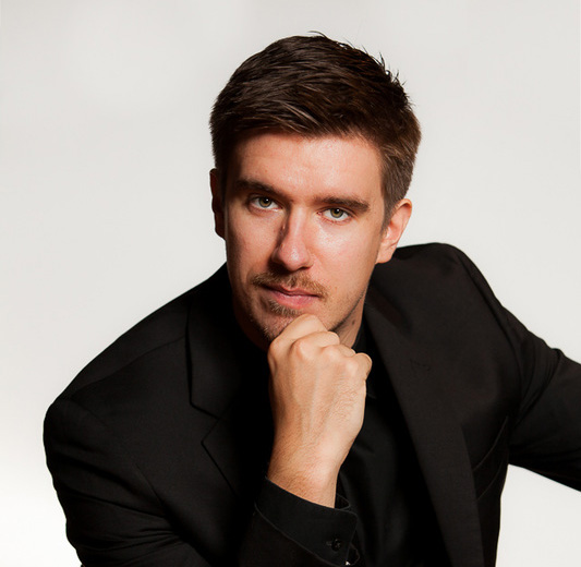 white man sitting with one hand on his chin wearing a black shirt