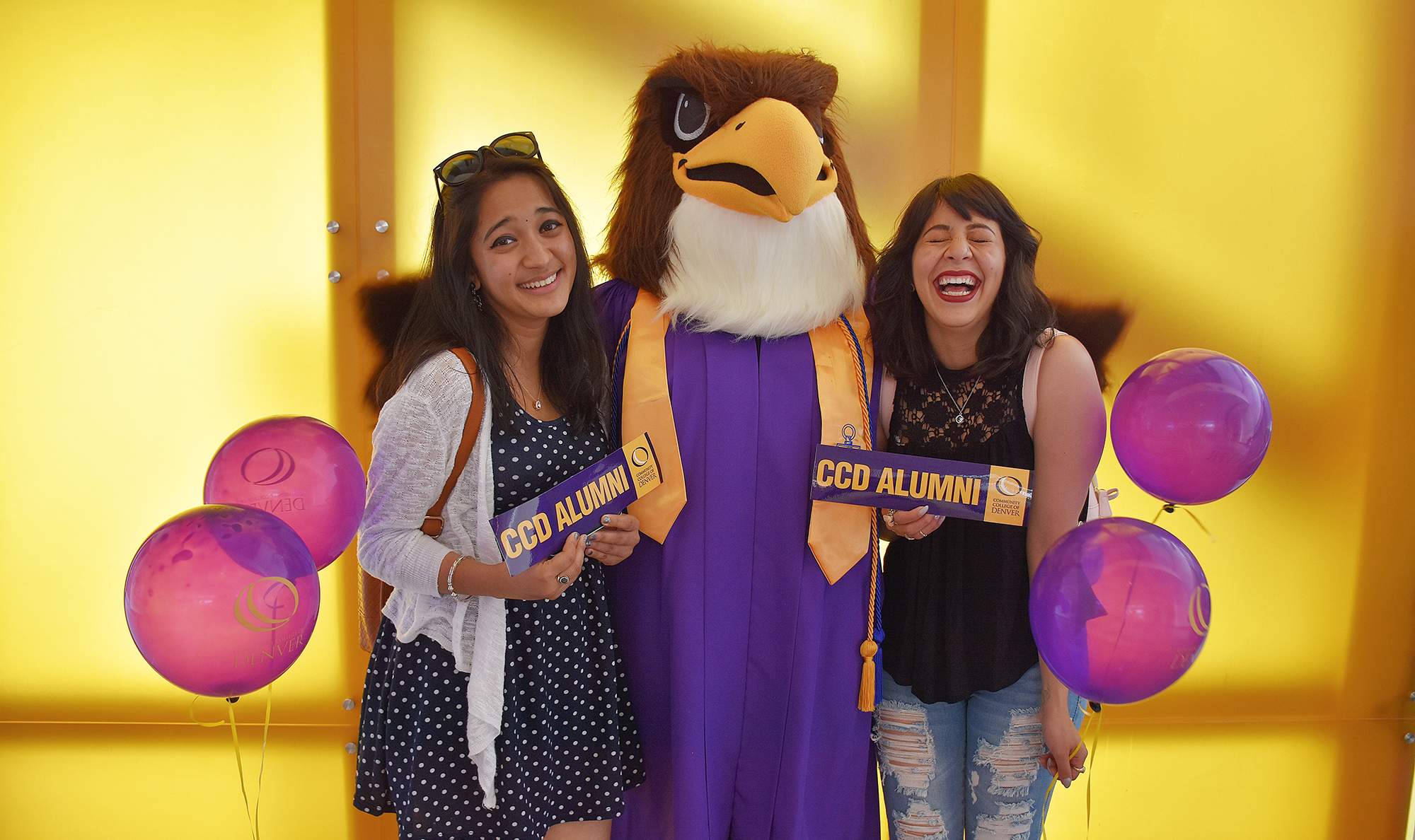 Two CCD Students holding an Alumni bumpersticker with the mascot