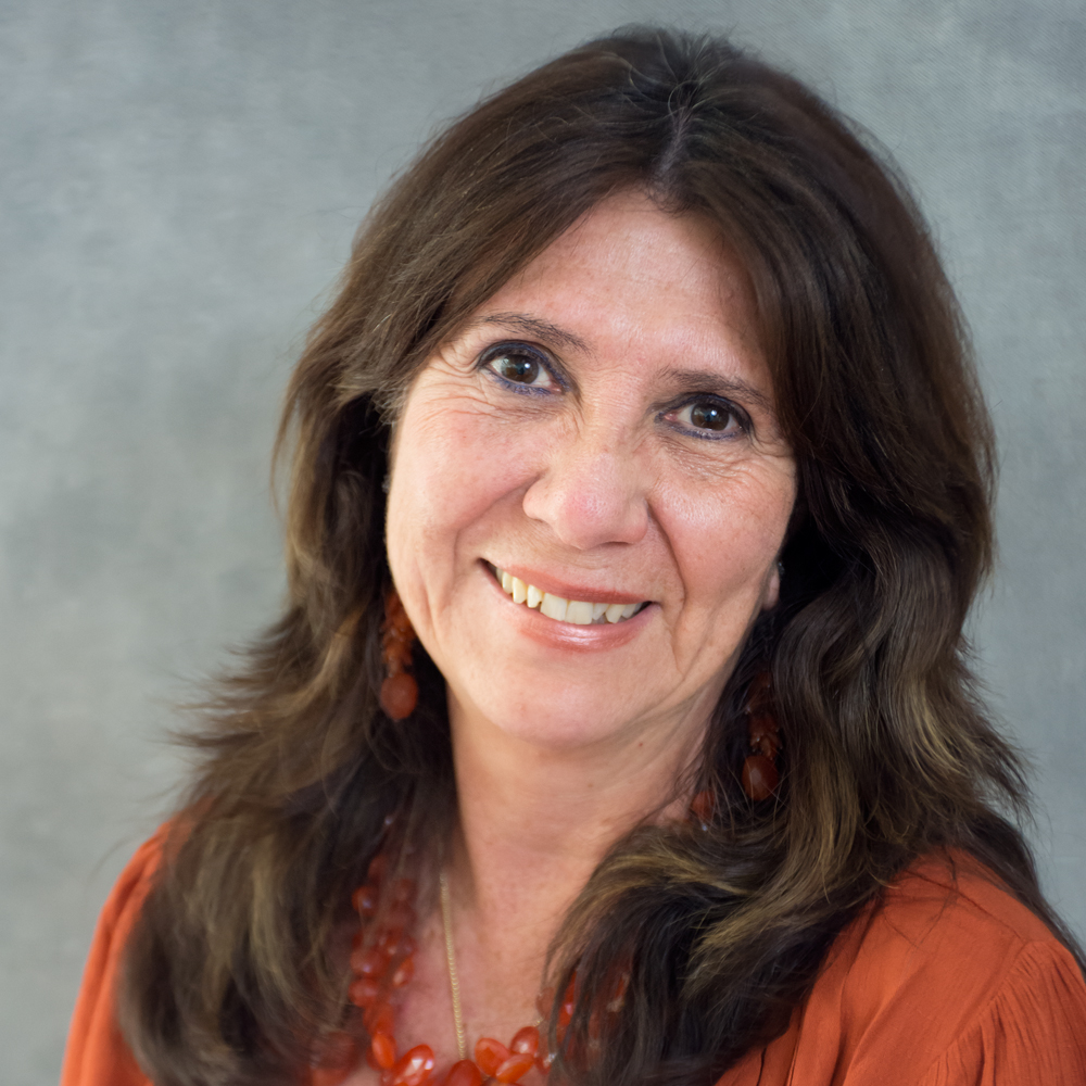 Smiling person with shoulder length dark brown hair wearing orange beads and orange top