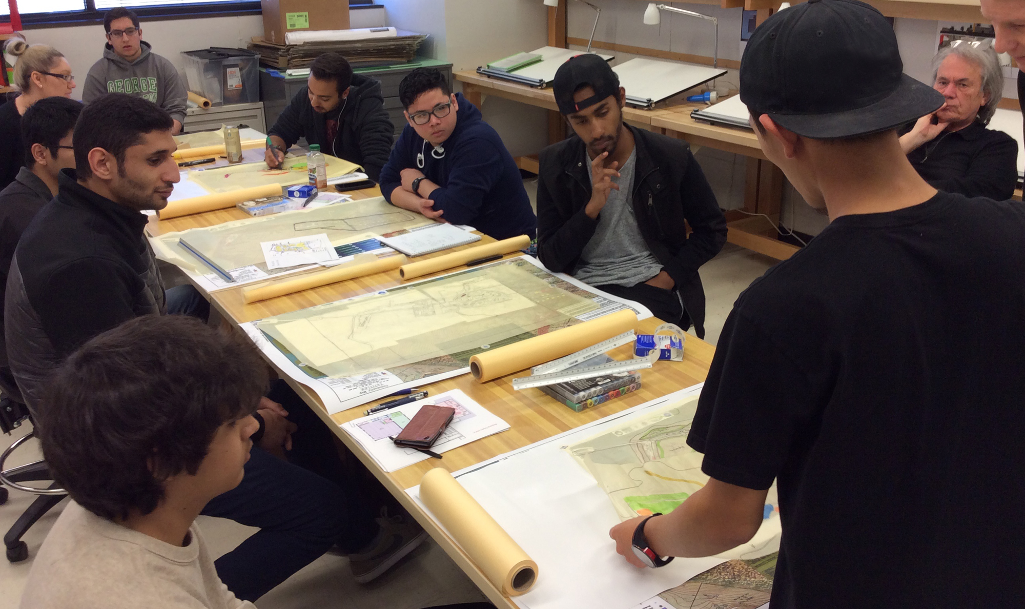 students around a design table with drafting designs