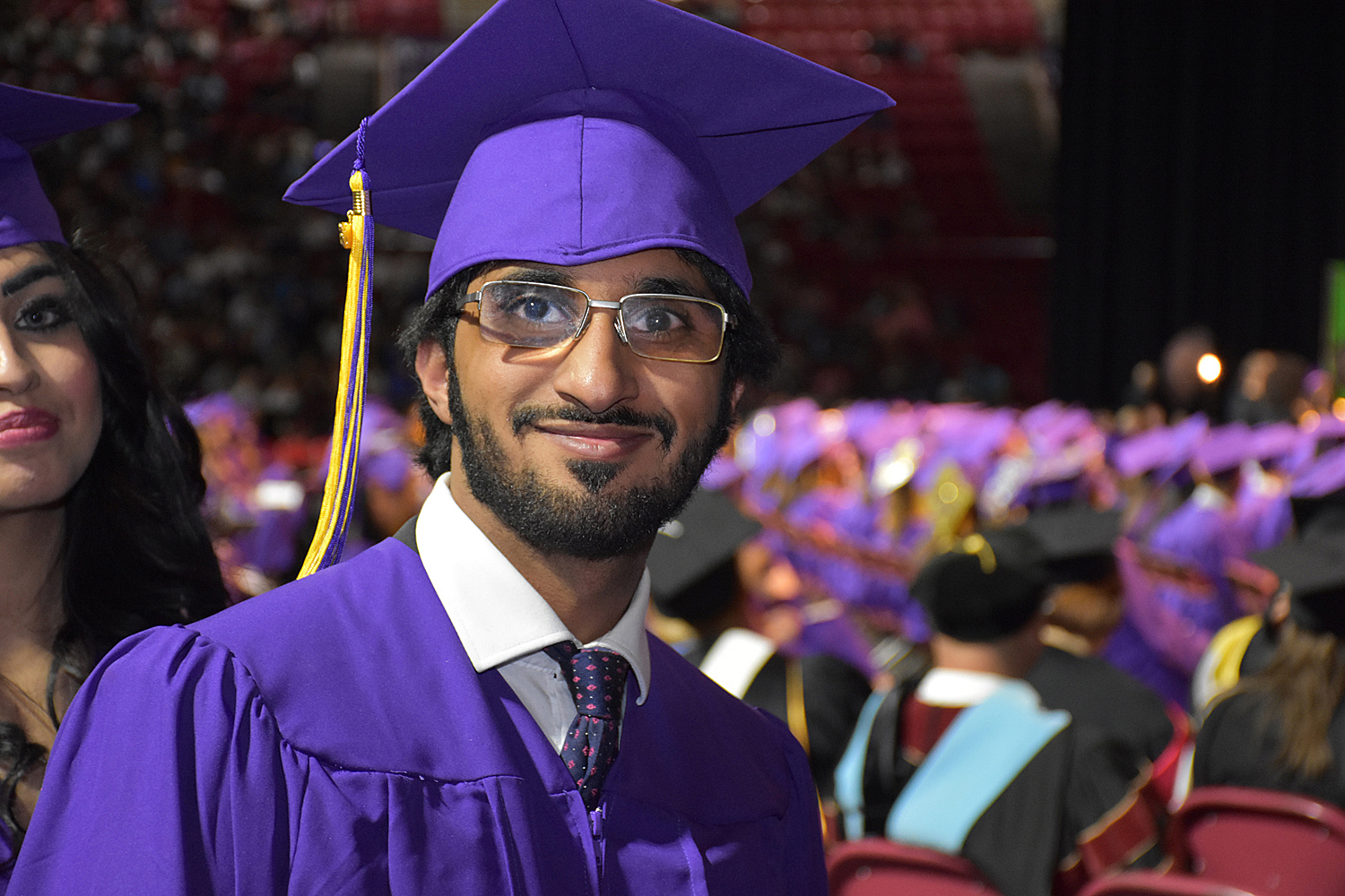 male graduate wearing purple cap and gown smiles proudly