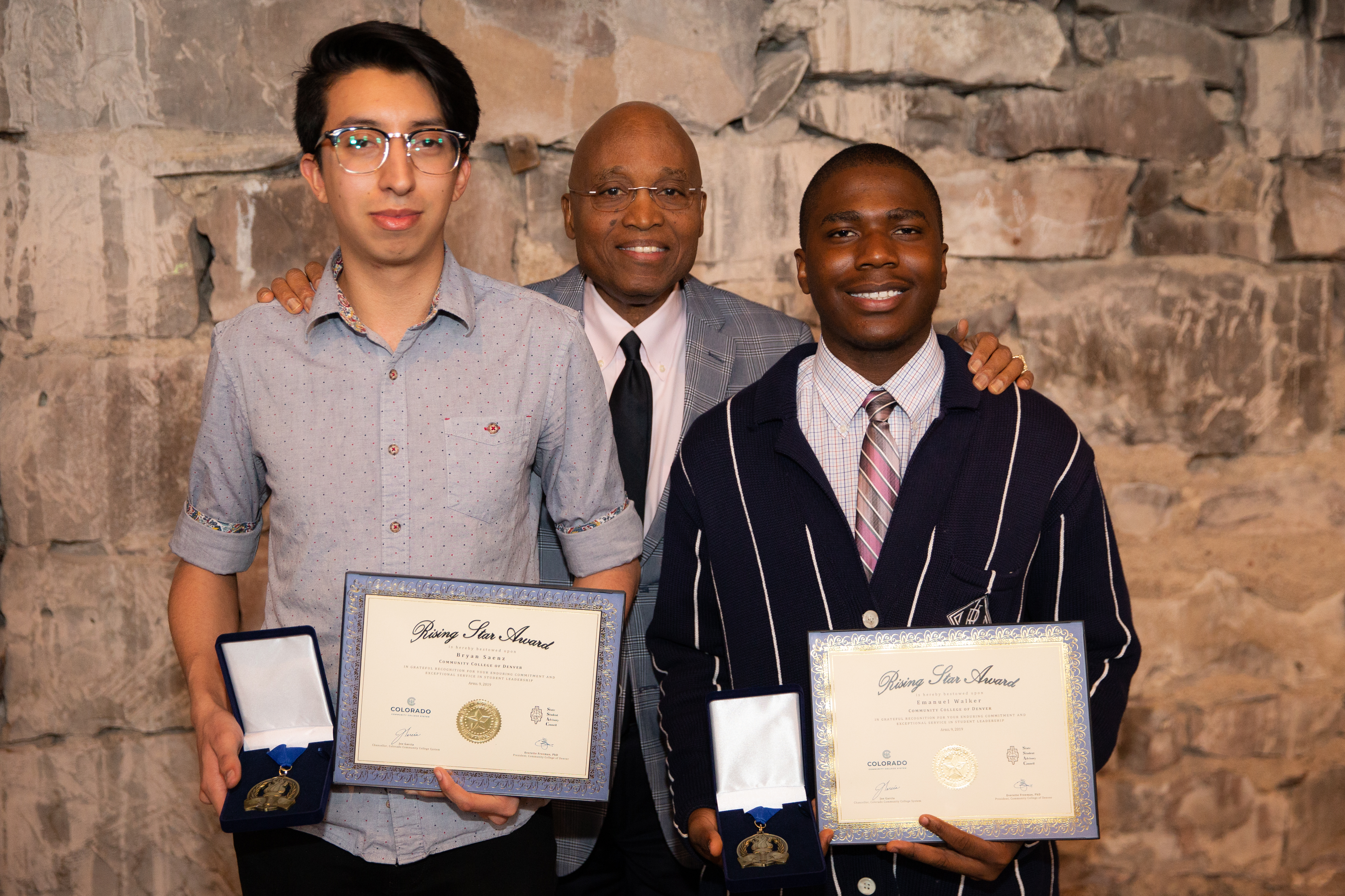 two students holding certificates and awards with the president of the college