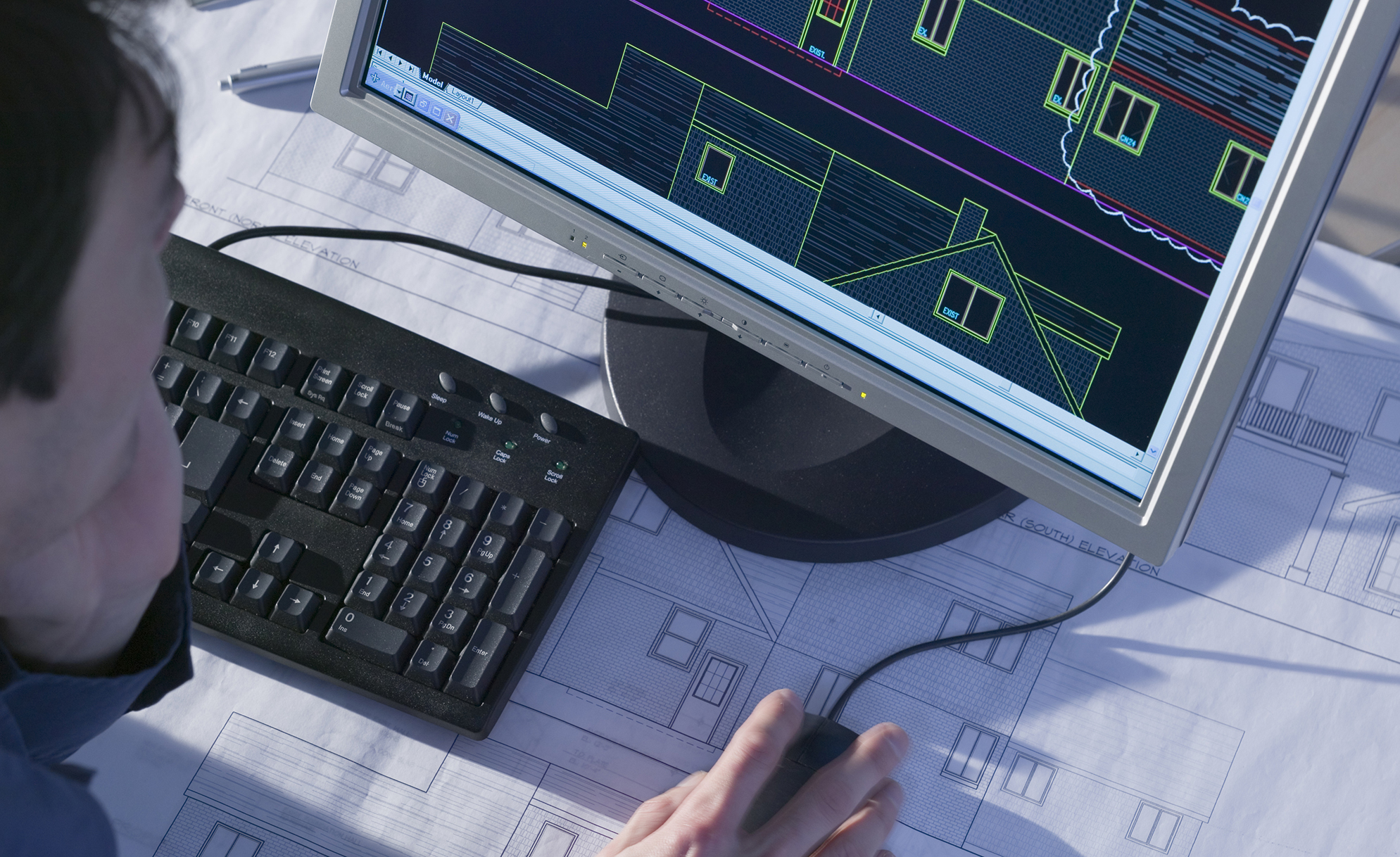 image of the hands of a male student working on computer drafting and blueprints.