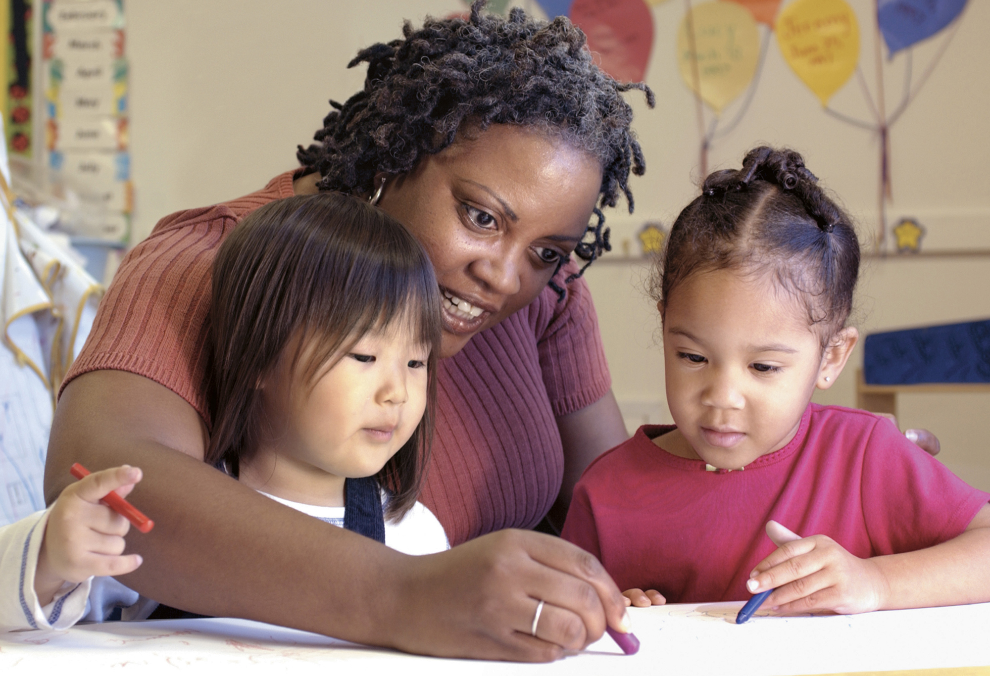 image of female teacher coloring with two pre-school girls