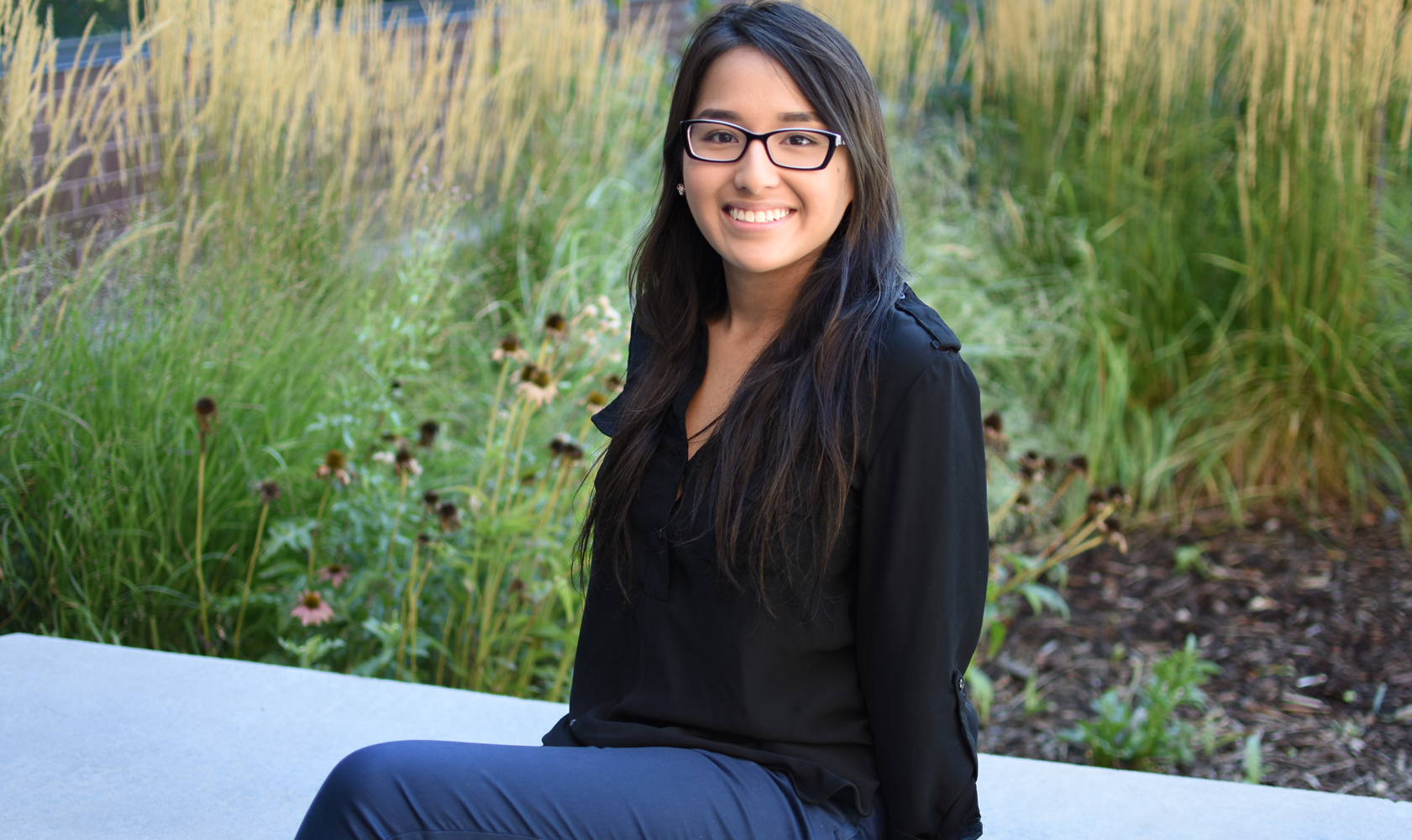 smiling student with glasses sits outside