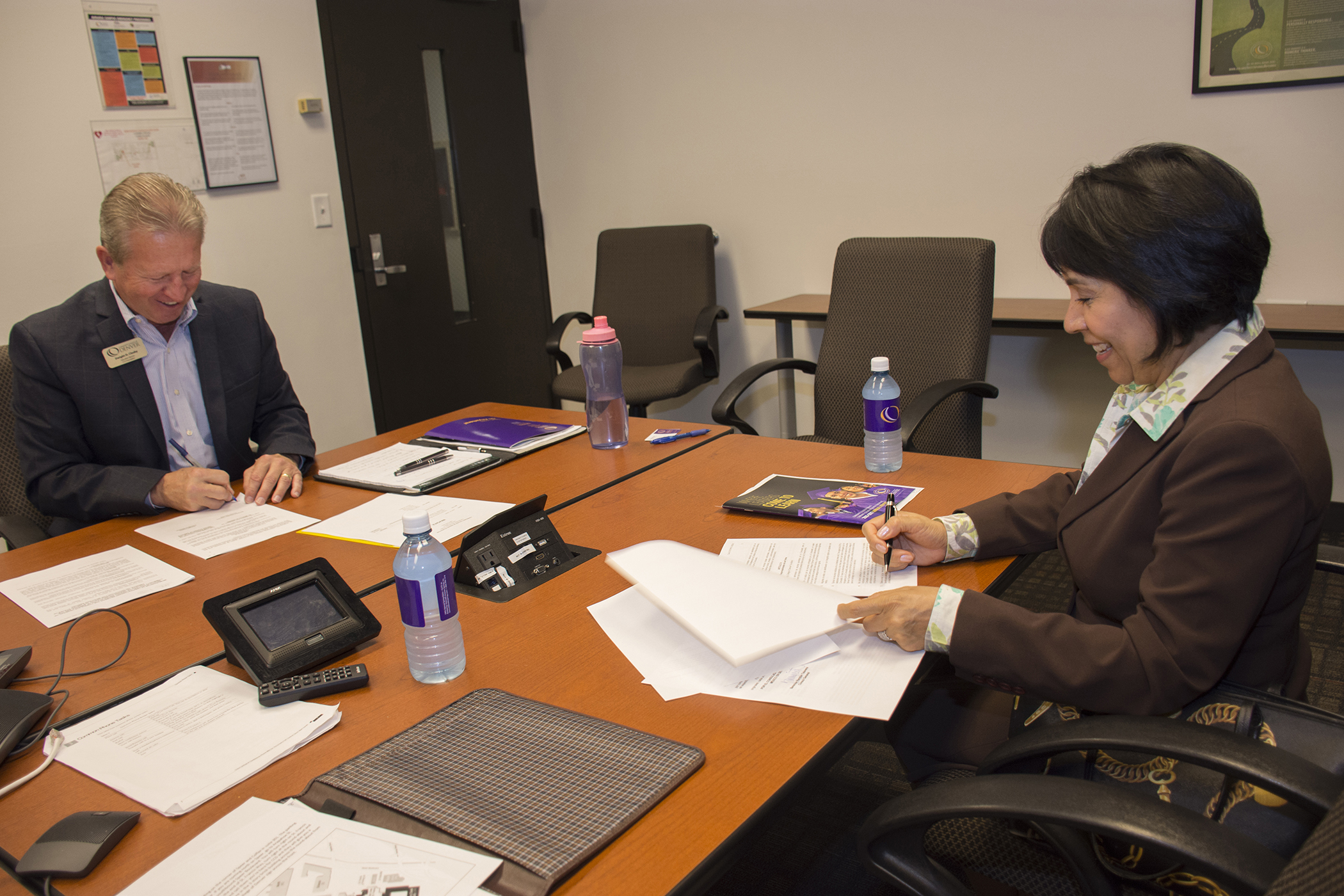 white male and Hispanic woman sitting across from eachother signing a document
