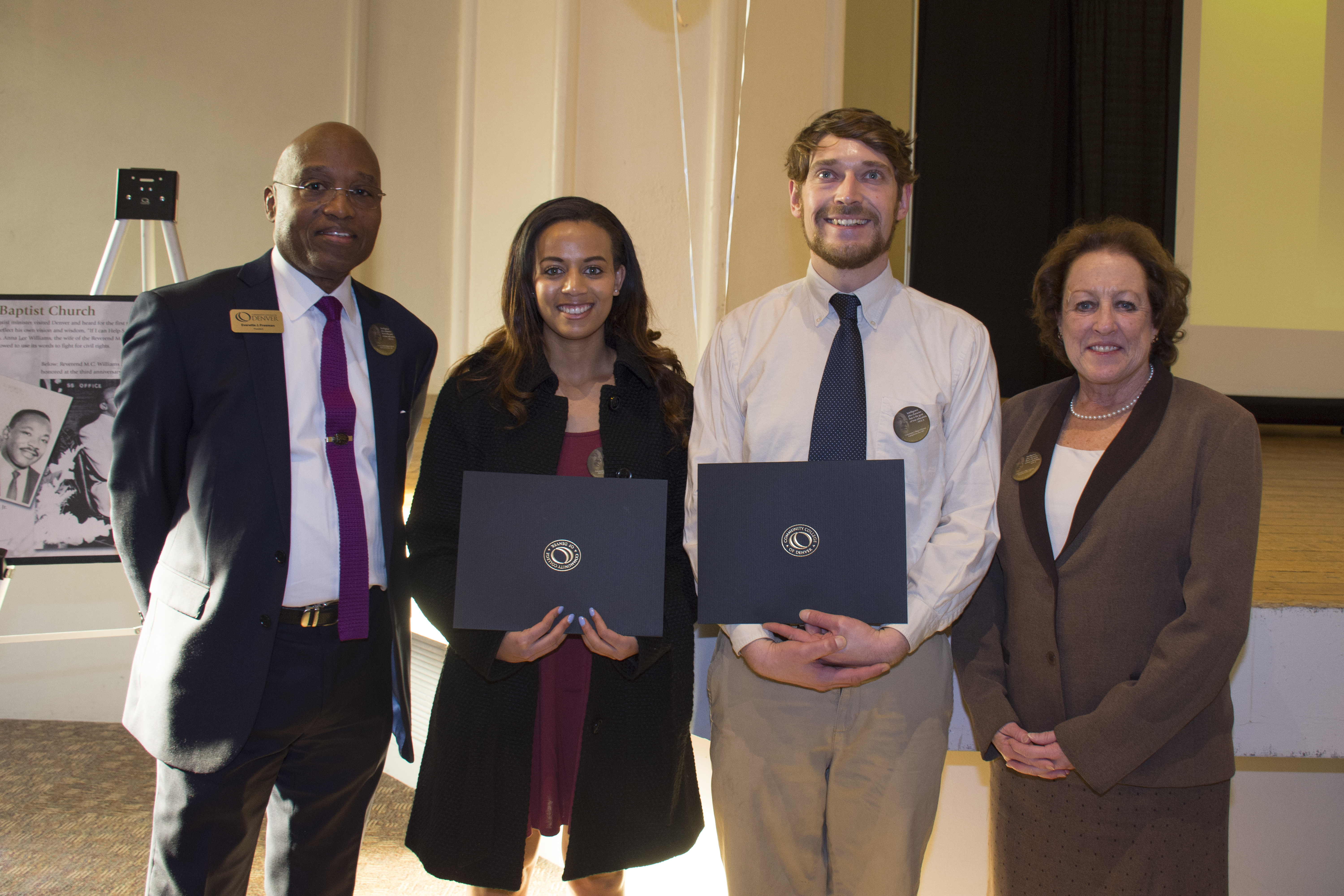 two students holding scholarship awards with the president of the college and system office