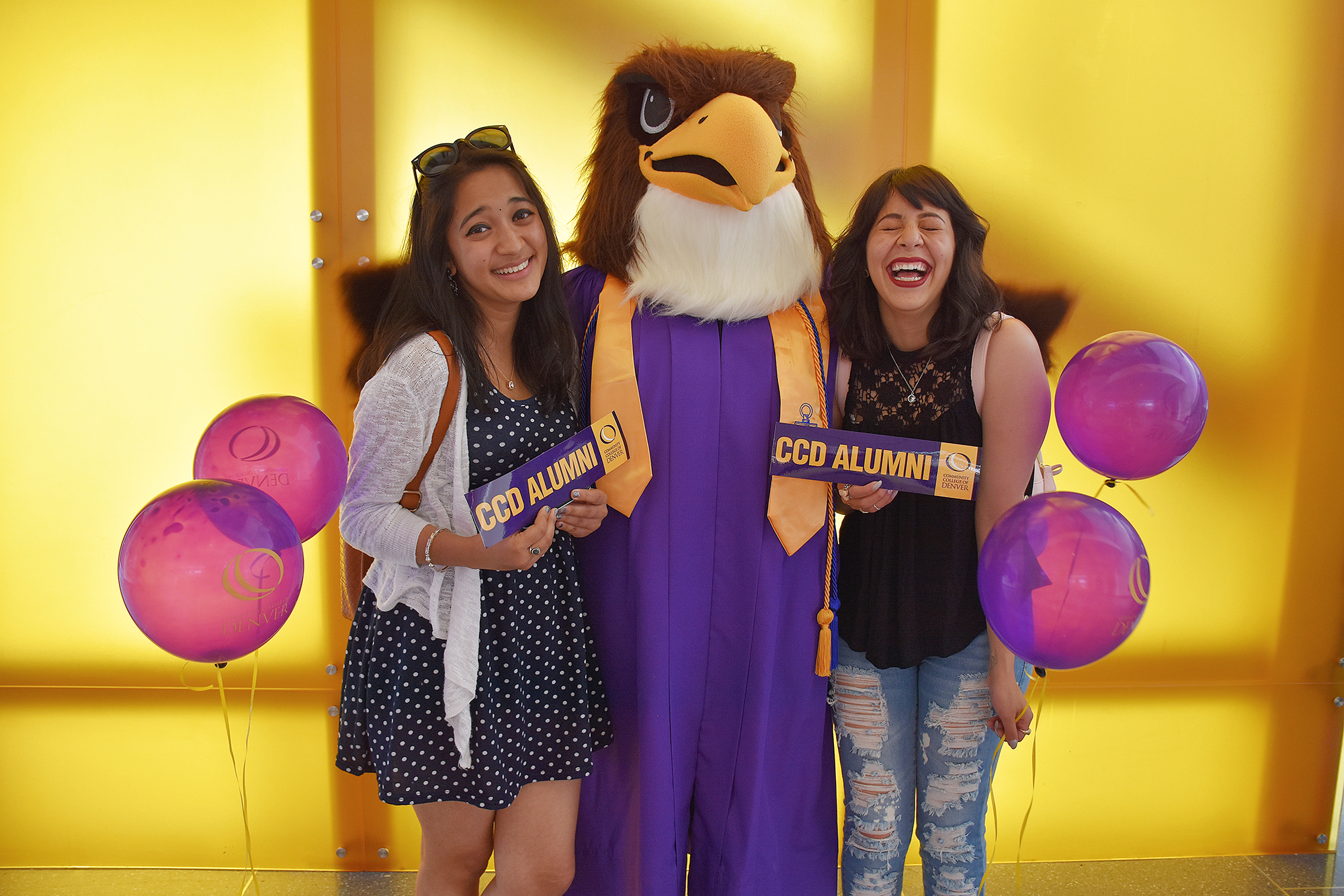 two women holding CCD Alumni bumperstickers with Mascot