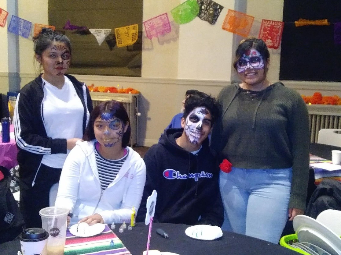 Students enjoying the face painting at Dia De Los Muertos four students 3 girls and one boy with their faces painted in sugar skull designs