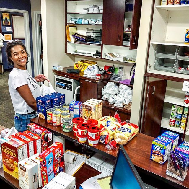young women standing in front of food pantry food items smiling