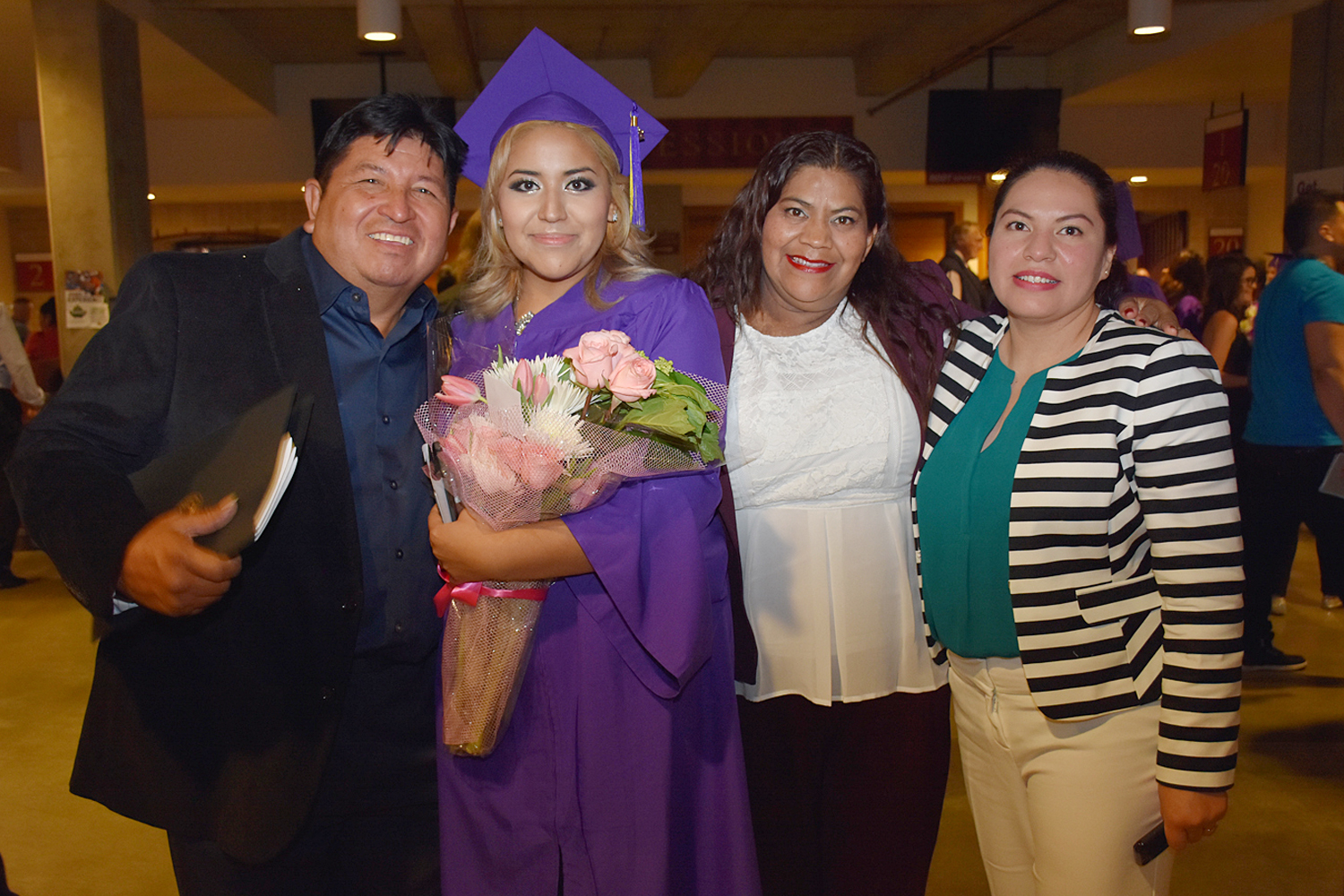 woman holding flowers stands with friends and family after graduations