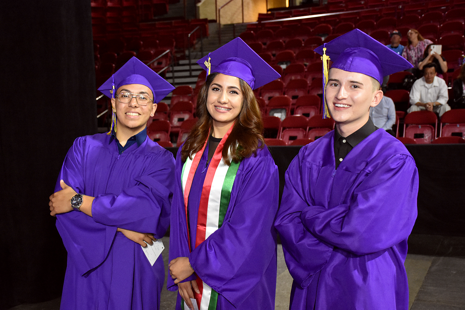 three students in purple cap and gowns standing at graduation