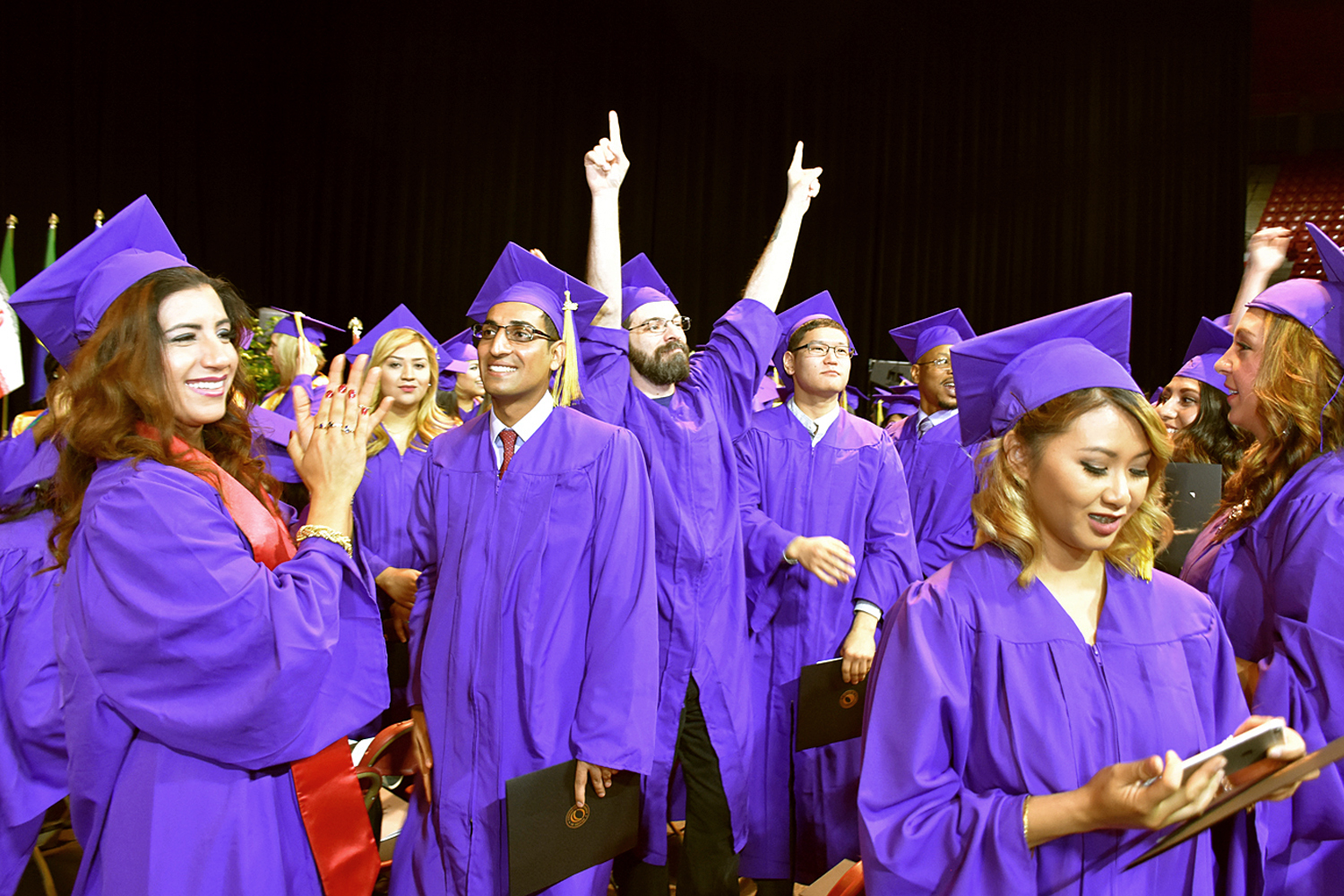 people in purple caps and gowns celebrate with clapping and hands raised in celebration