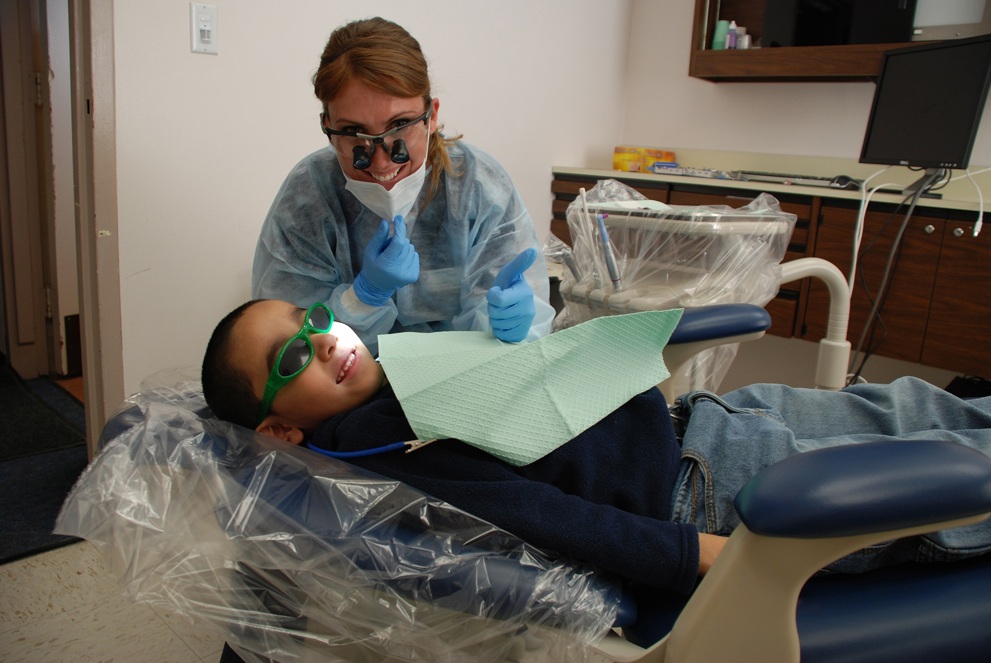 A dental hygienist giving a thumbs up with a smiling young patient