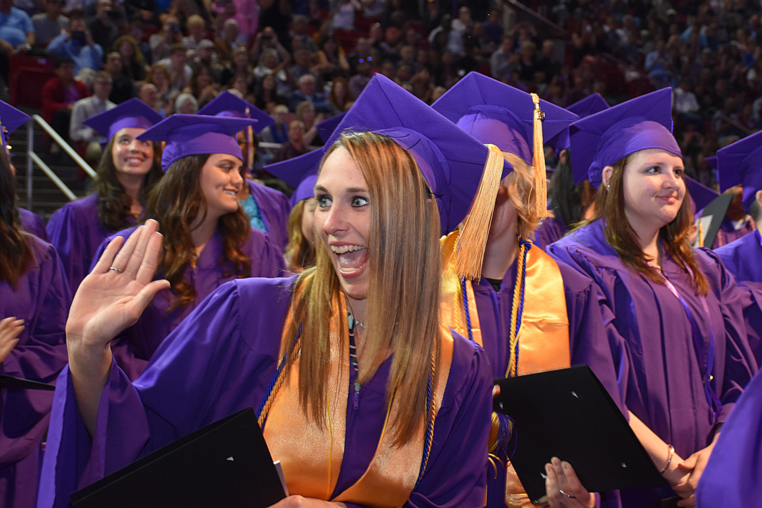 woman in purple cap and gown and gold sash receives a high five in celebration