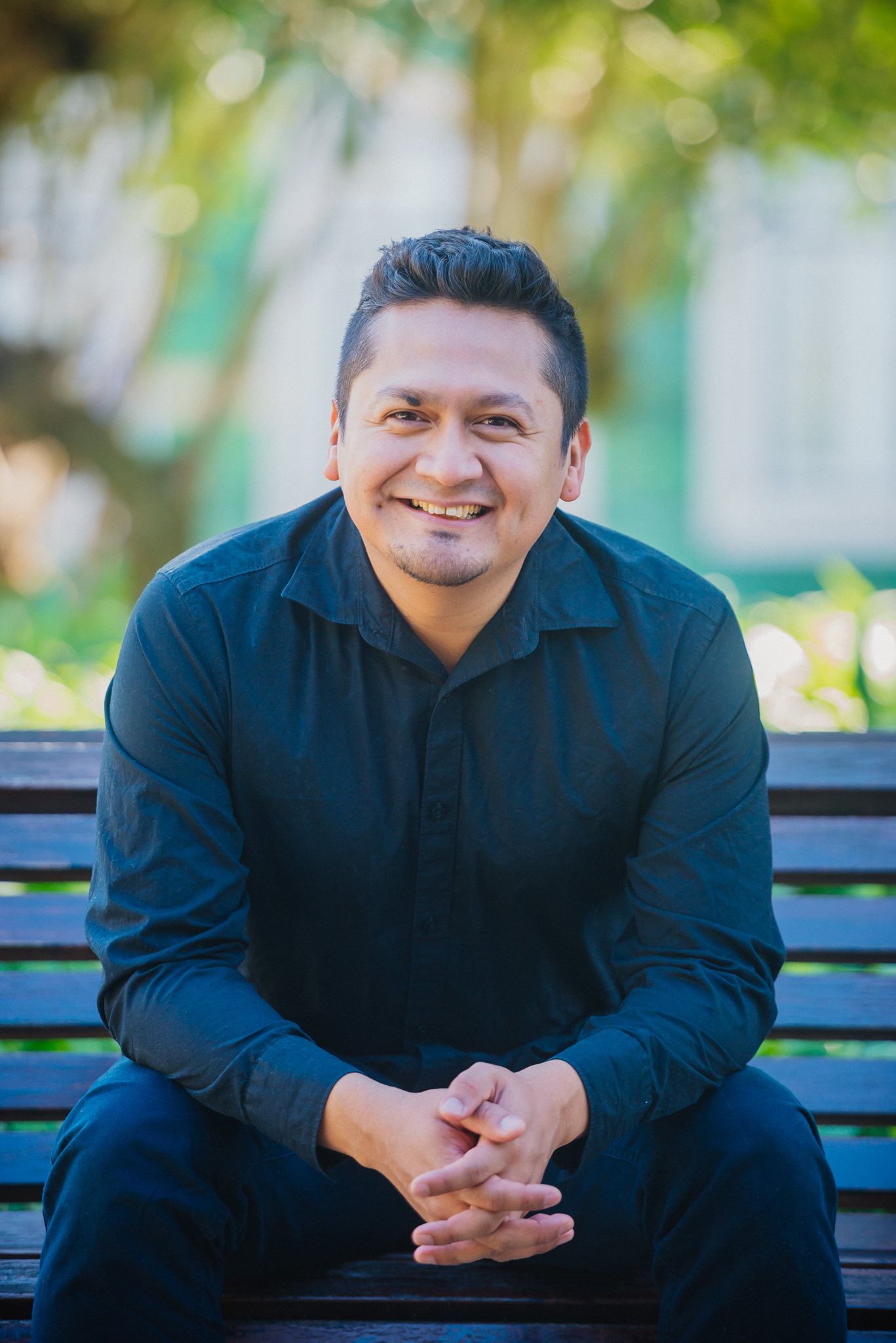 CCD Alumnus Jermaine Amado man wearing black button down sitting on a bench