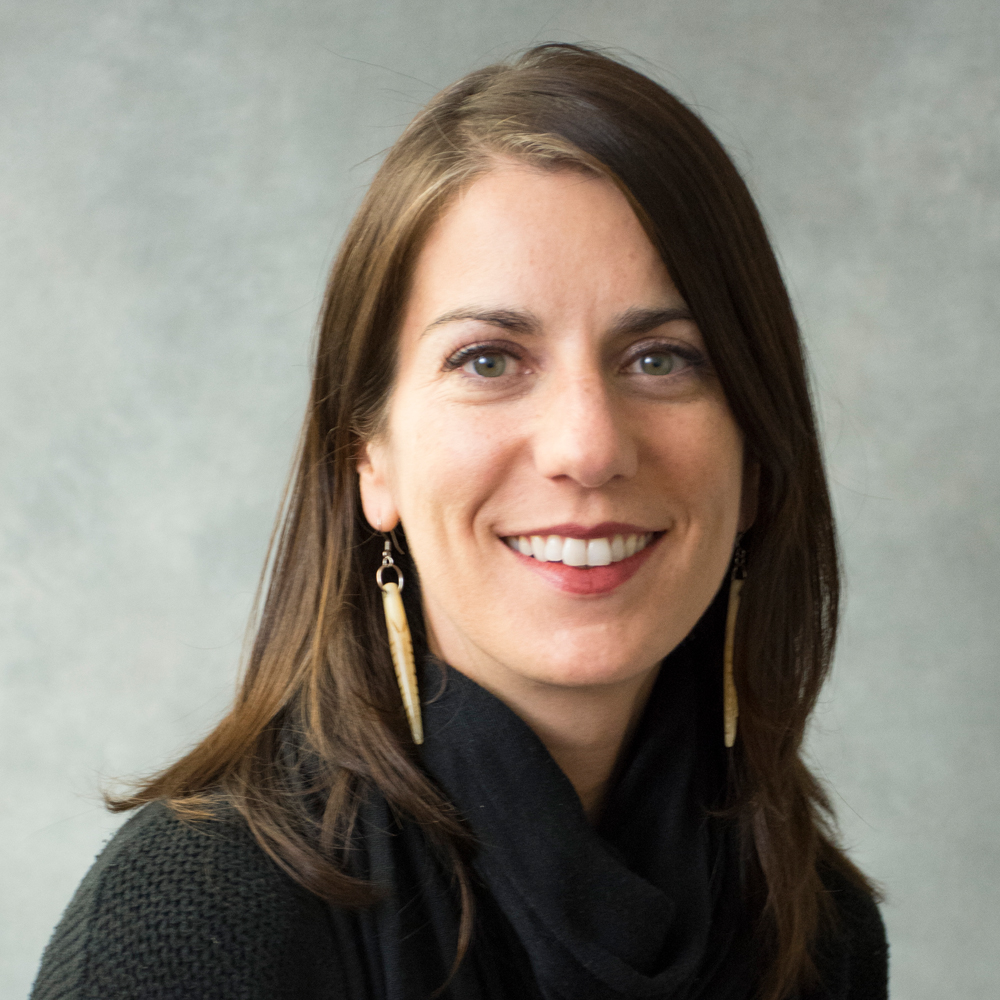 Smiling woman with medium length brown hair, wearing dangling gold earrings and black shirt