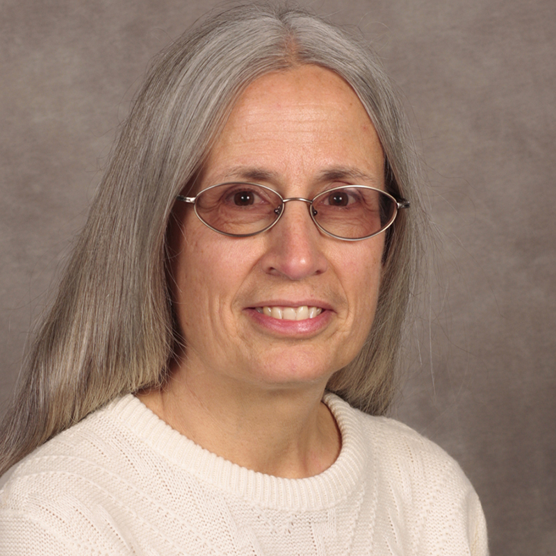 Woman with long silver hair wearing glasses and white sweater