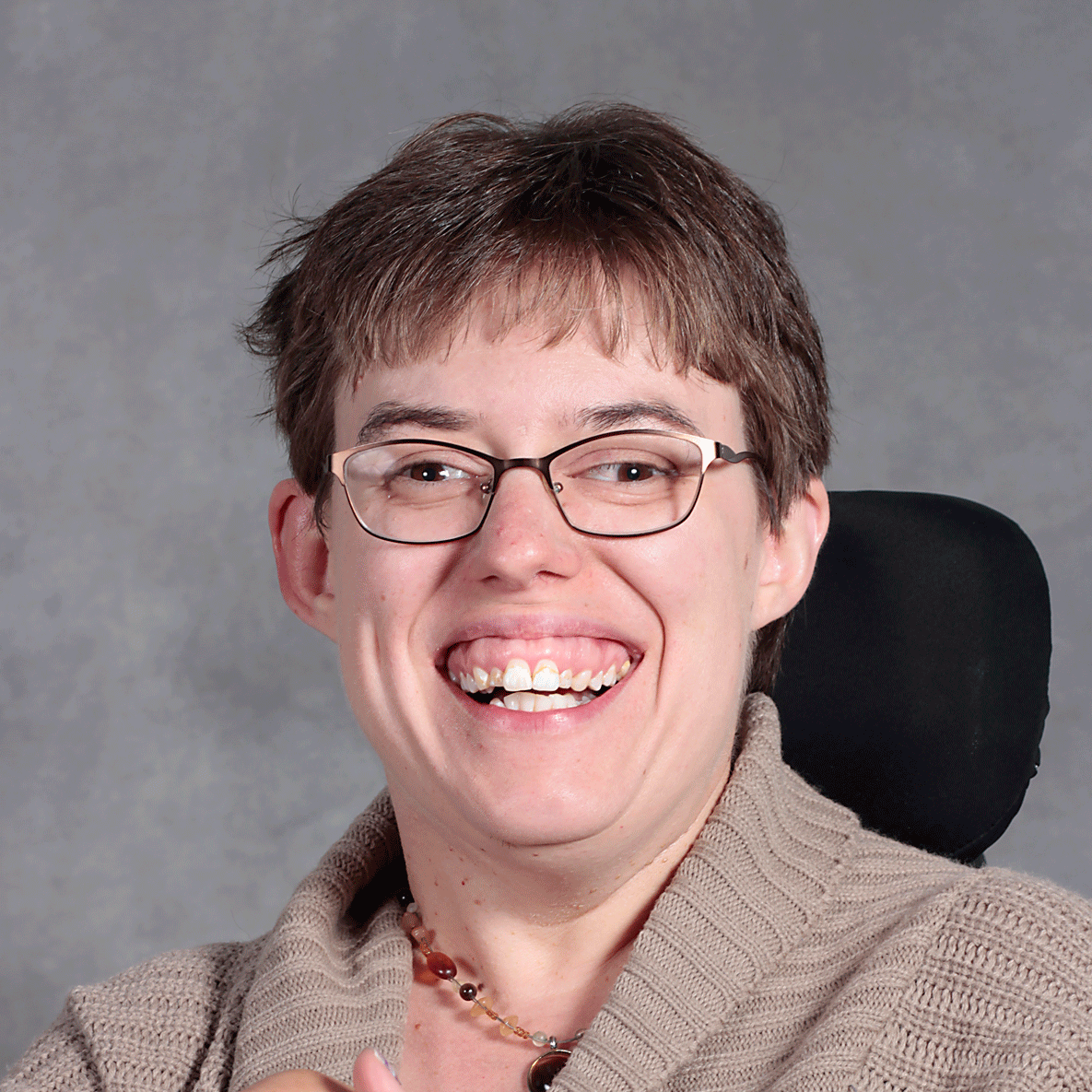 Smiling person with short brown hair and bangs wearing glasses and a tan sweater