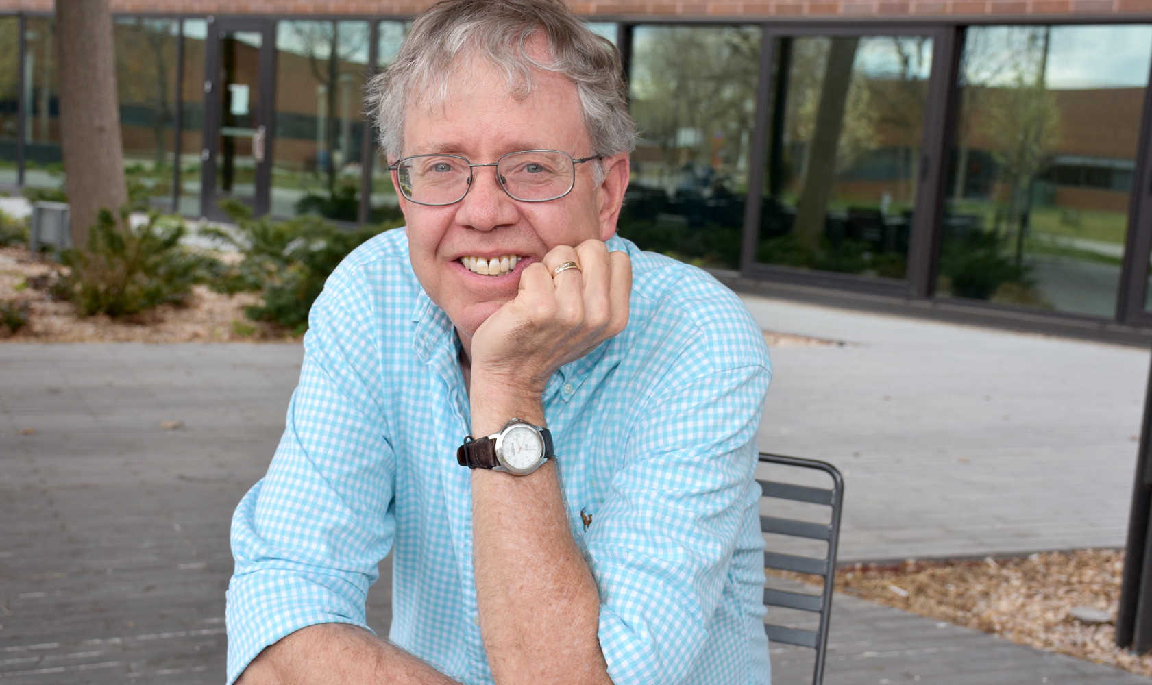 a picutre of a man in a light blue shirt leaning on his hand smiling