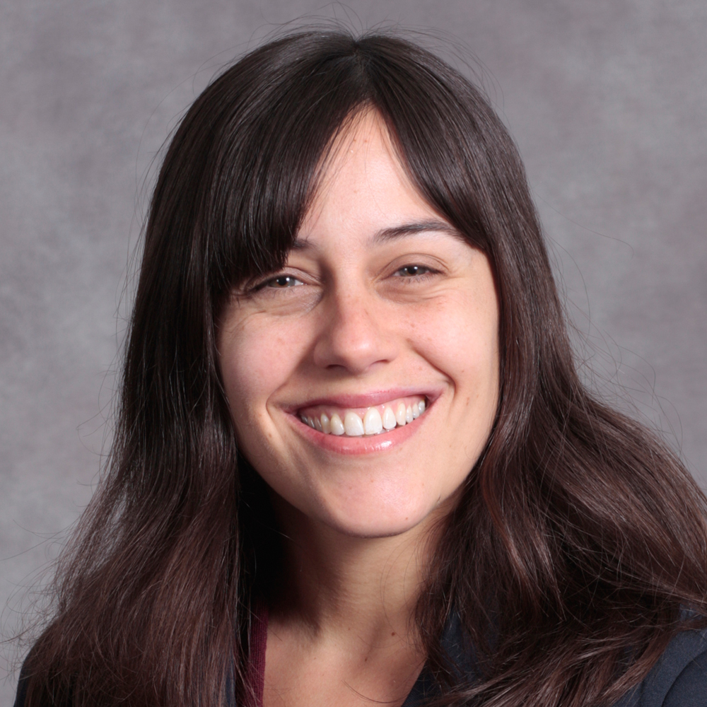 Smiling person with medium length dark brown hair wearing a dark top