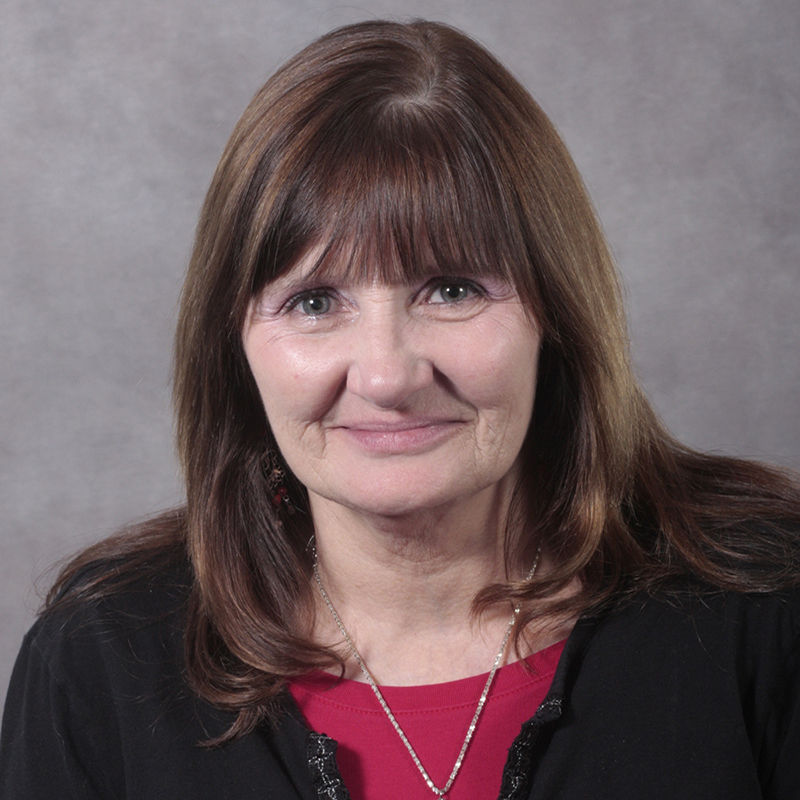 Person with shoulder-length brown hair and bangs wearing a red top and black sweater