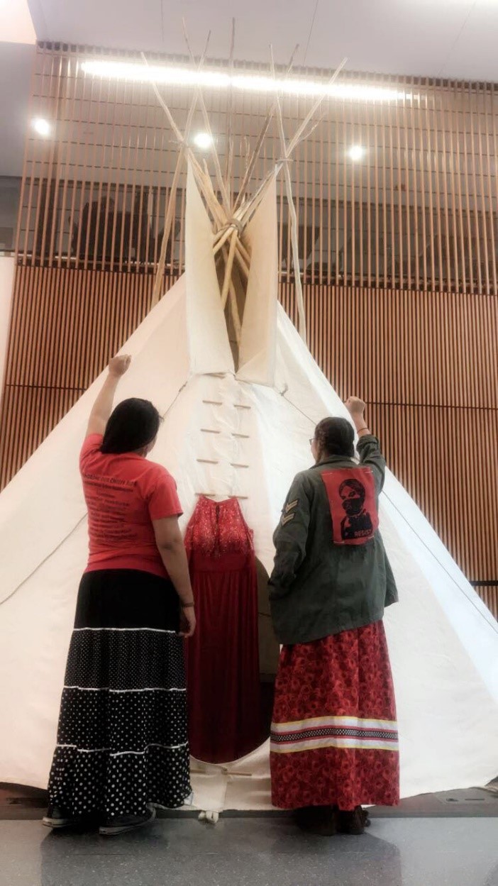REDress Project Dress representing murdered or missing Indigenous Women. Two Females with fists raised in front of a tipi