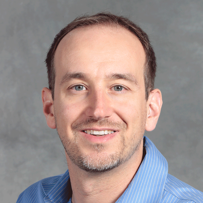 Smiling man with short brown hair wearing a blue shirt