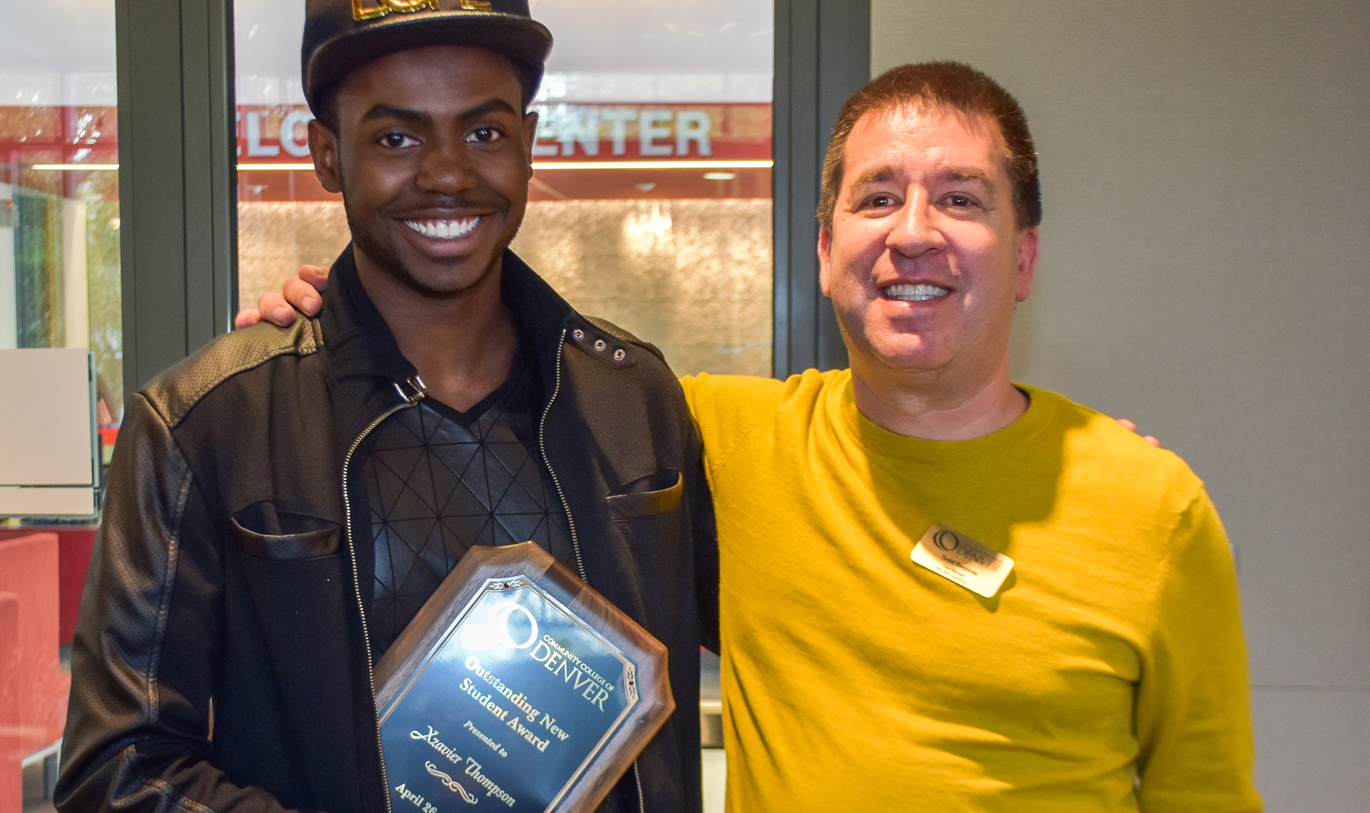 two men smiling, one holding an award