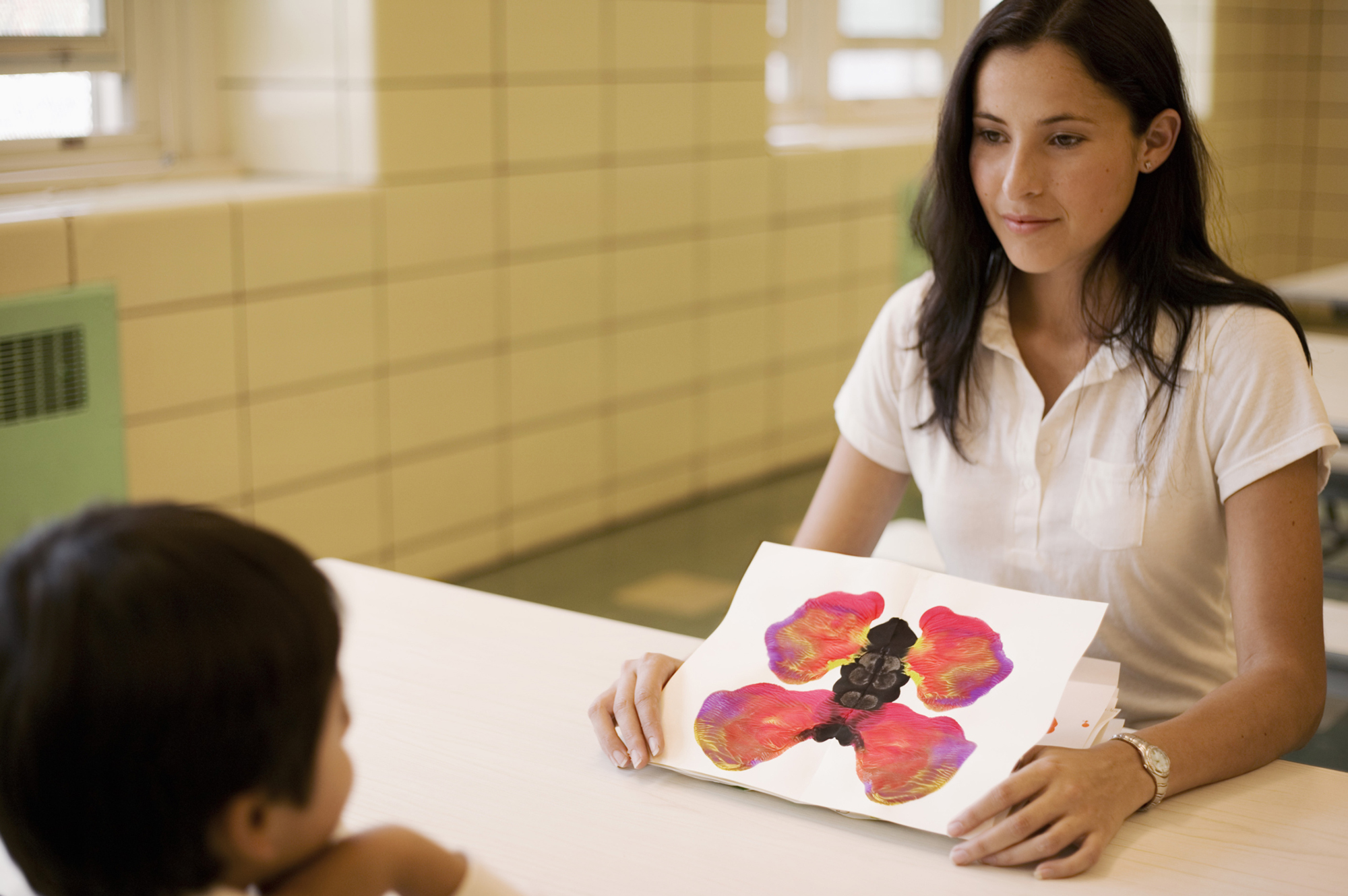 Woman showing a kid an ink blot test that looks like a butterfly
