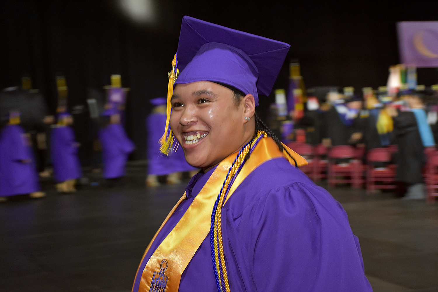 person wearing purple cap and gown and yellow sash indicating honor society