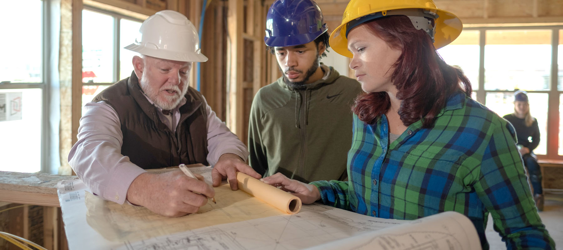 a male student and a female student look at blueprints with a man at a construction site