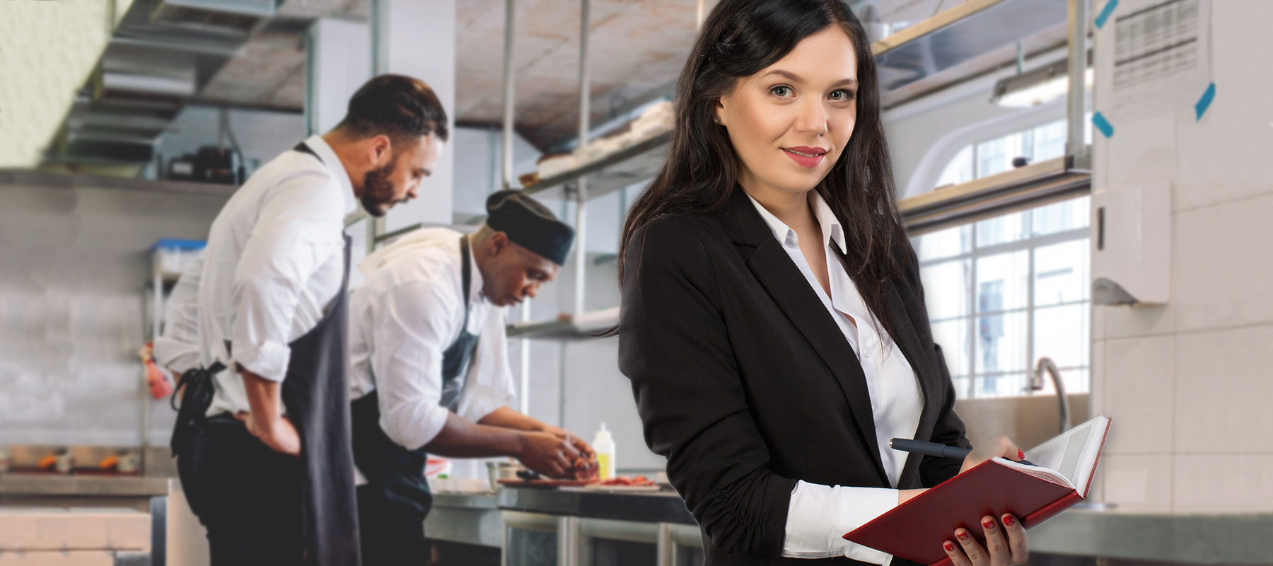 woman with a clipboard stands in a kitchen with two chefs cooking in the background