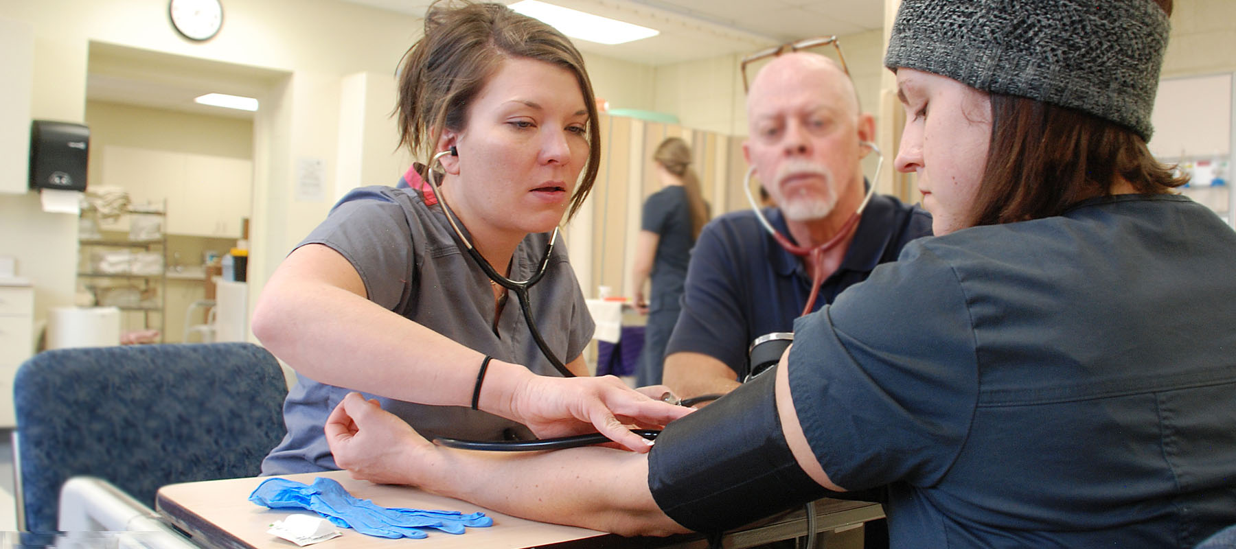 students in scrubs practicing taking a patient's blood pressure