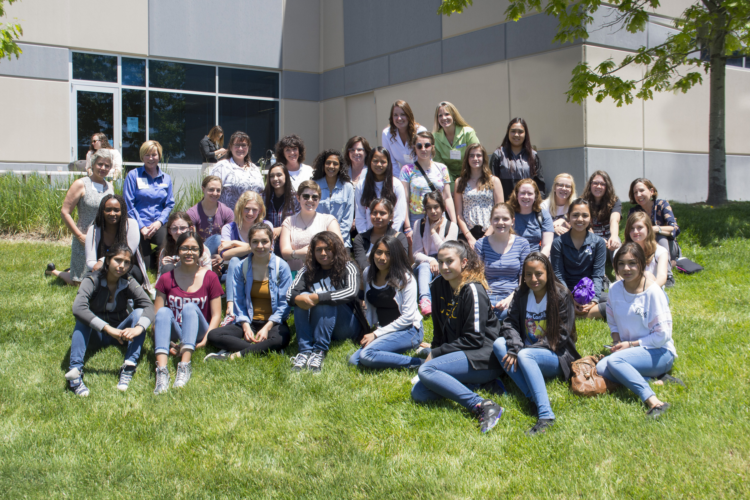 group of female students sitting on the grass outside a building