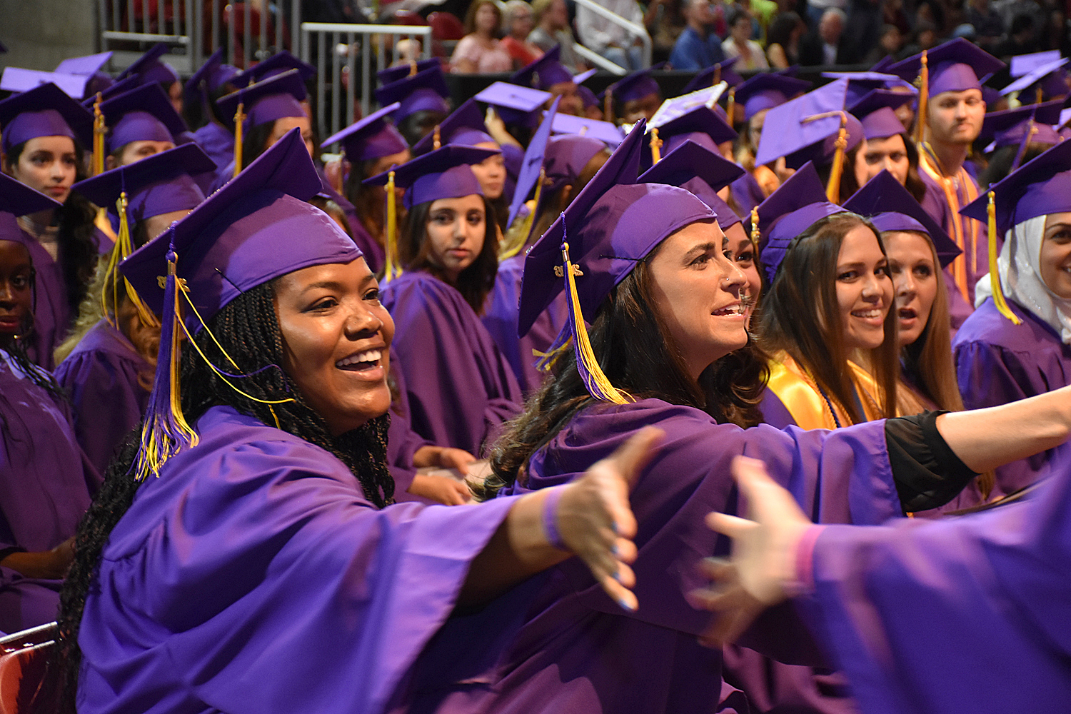 students in purple caps and gowns shake hands in celebration