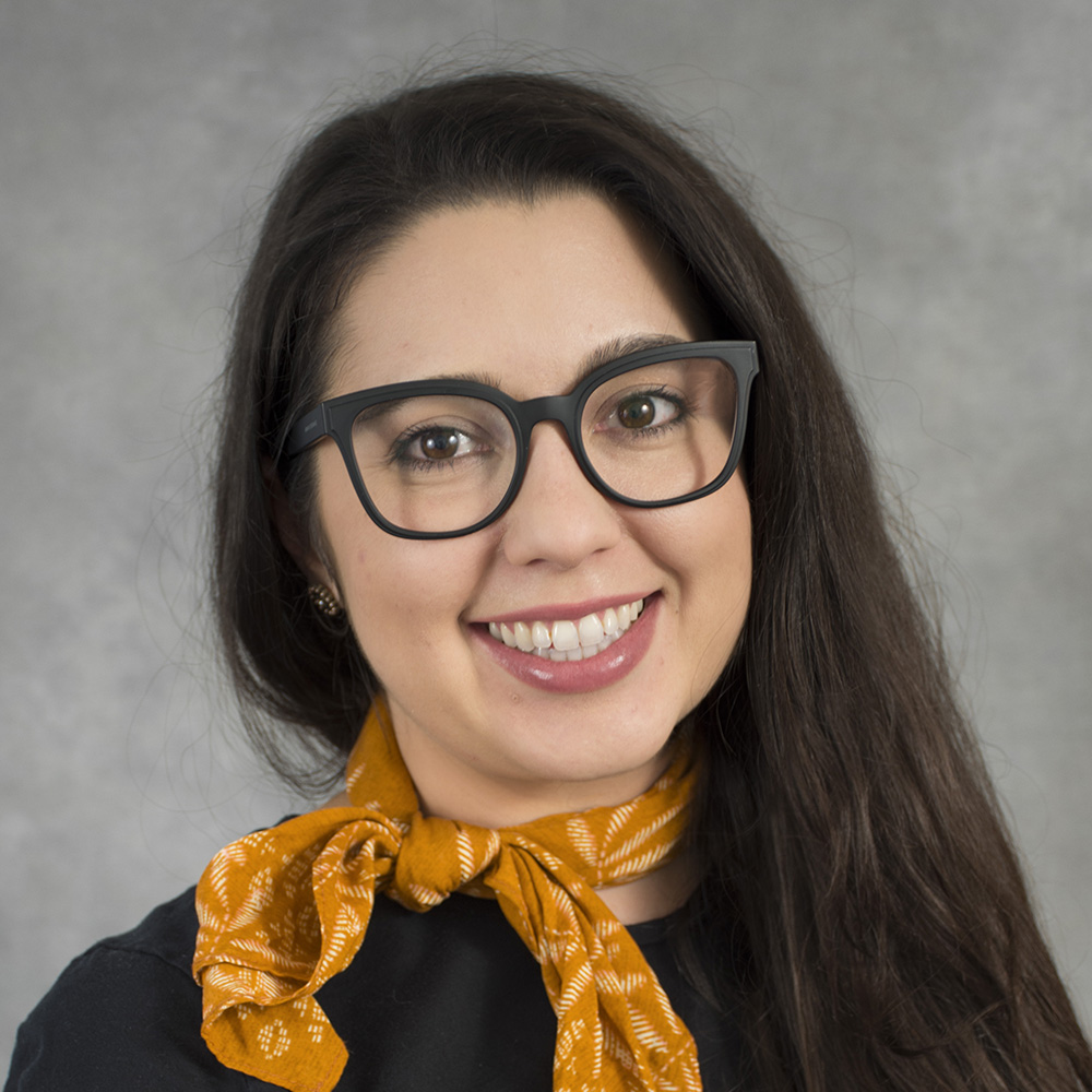 Smiling person wearing black glasses and gold scarf.