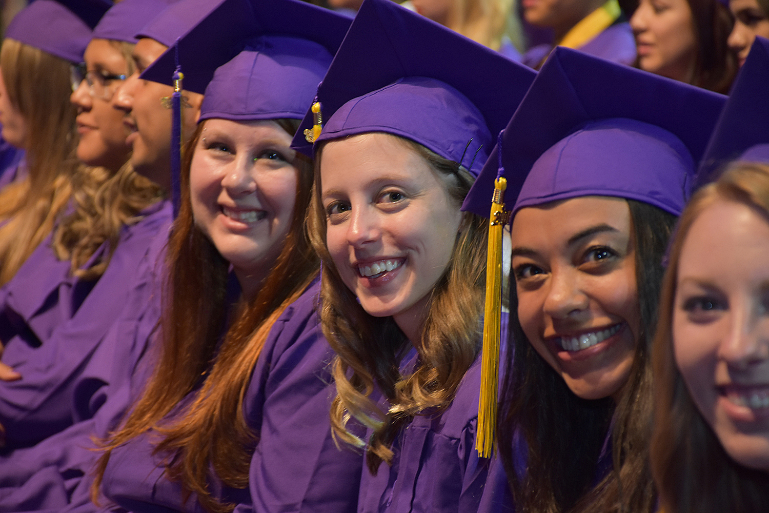 four women sit in a row in purple caps and gowns