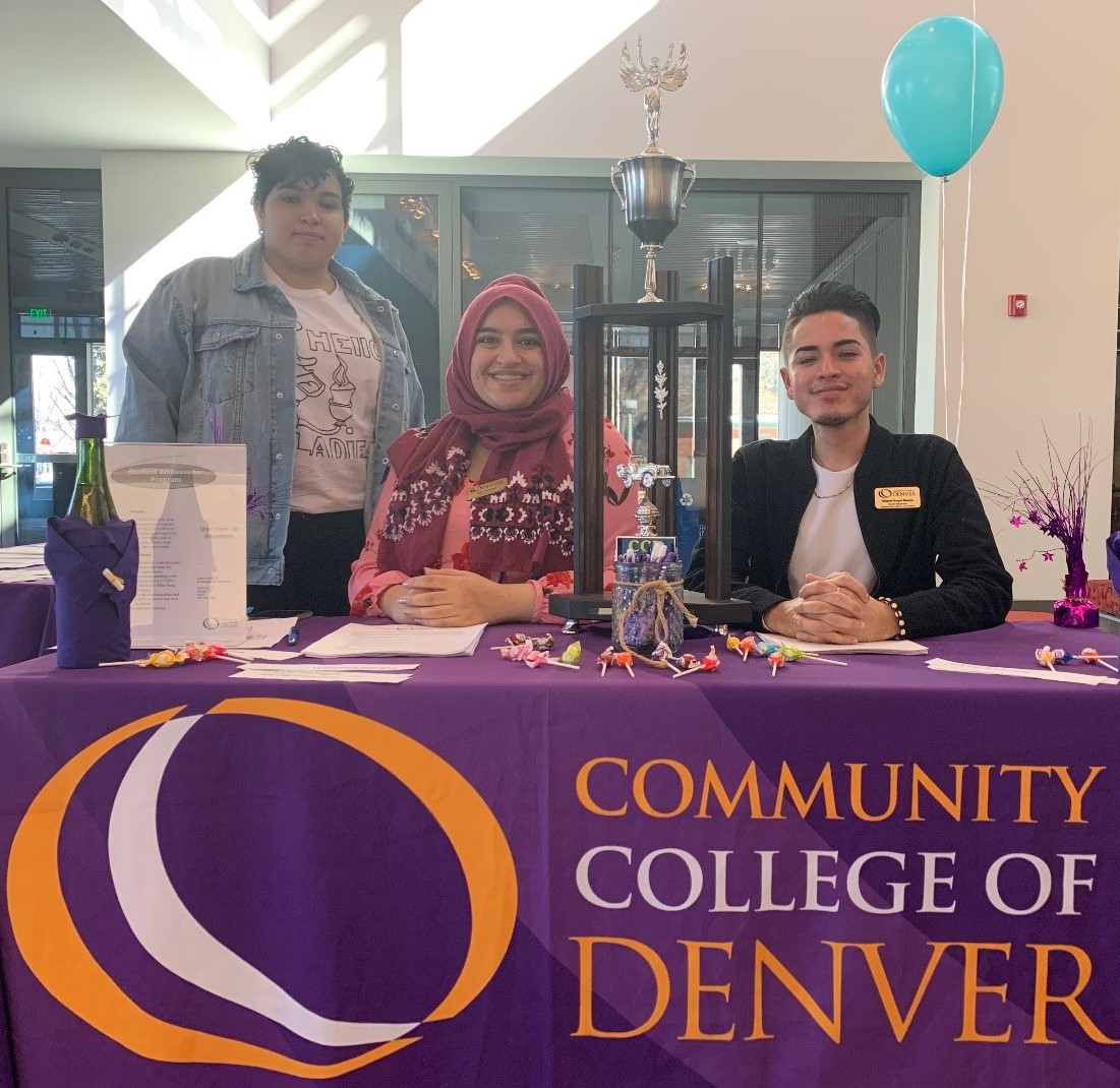 Three students one in a jean jacket, second with a pink shirt and 3rd black jacket all sitting at a table for CCD's workstudy fair