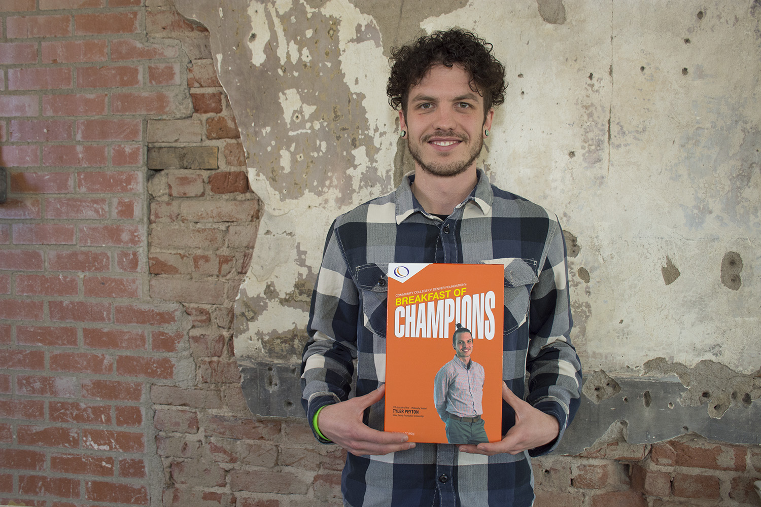 young man holding a box with his picture on it, in front of a brick background